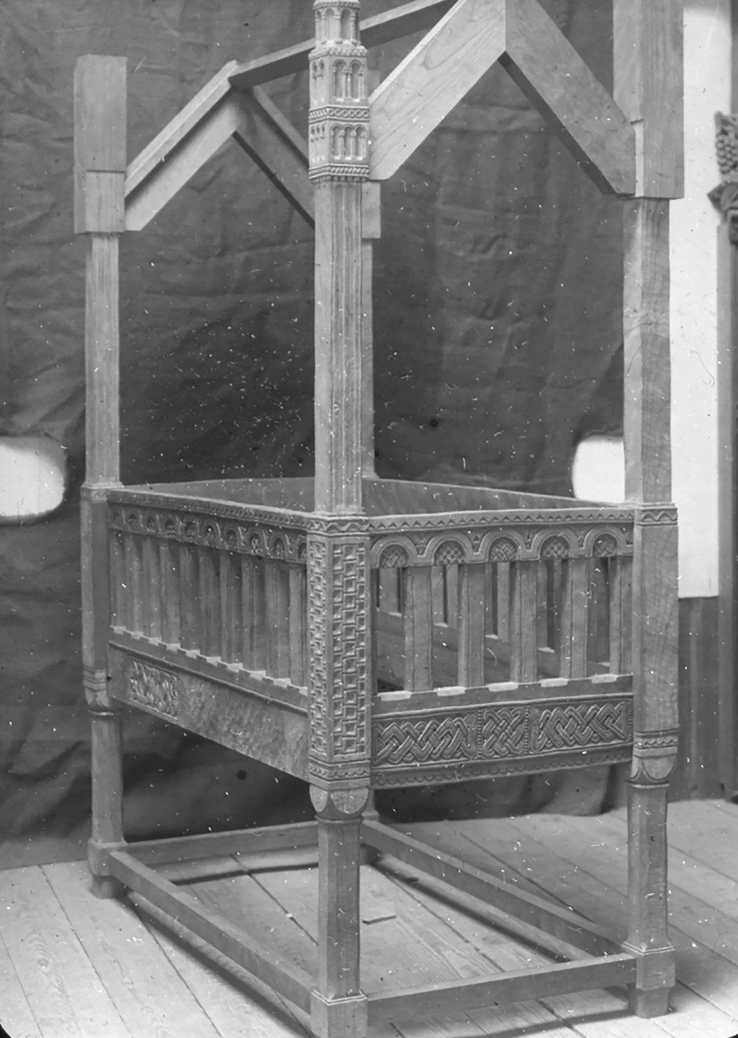 Figure 14: Archival photograph of Lachlan Pitcairn’s baby crib taken in one of the Bryn Athyn workshops. Some portions of the crib have been carved, while others are still unfinished. A closer look at some of the uncarved portions reveals the use of an adze to give the wood “irregularities similar to hand-hammered metal” (Cooke 1987, 315; see full quotation below).