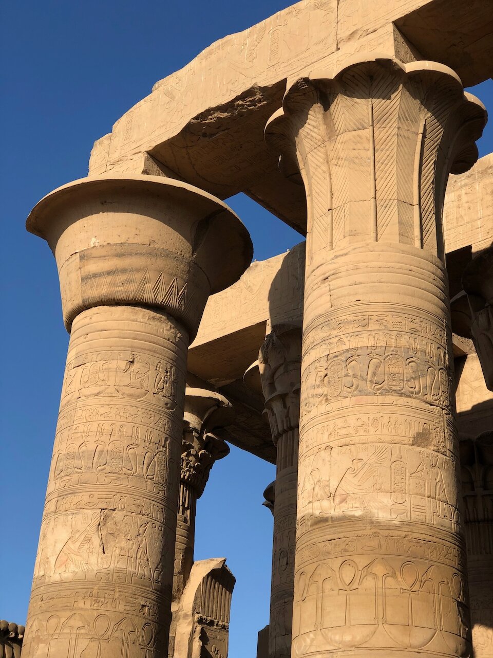 Two sand-colored columns stand before the backdrop of a deep blue sky and more temple remains.