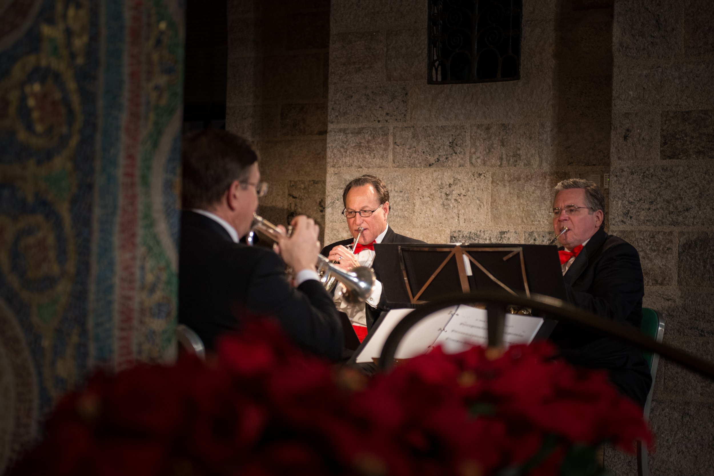  Three horn players perform during Glencairn Museum's annual Christmas Sing concert. Their red bowties complement the red poinsettias in the foreground. 