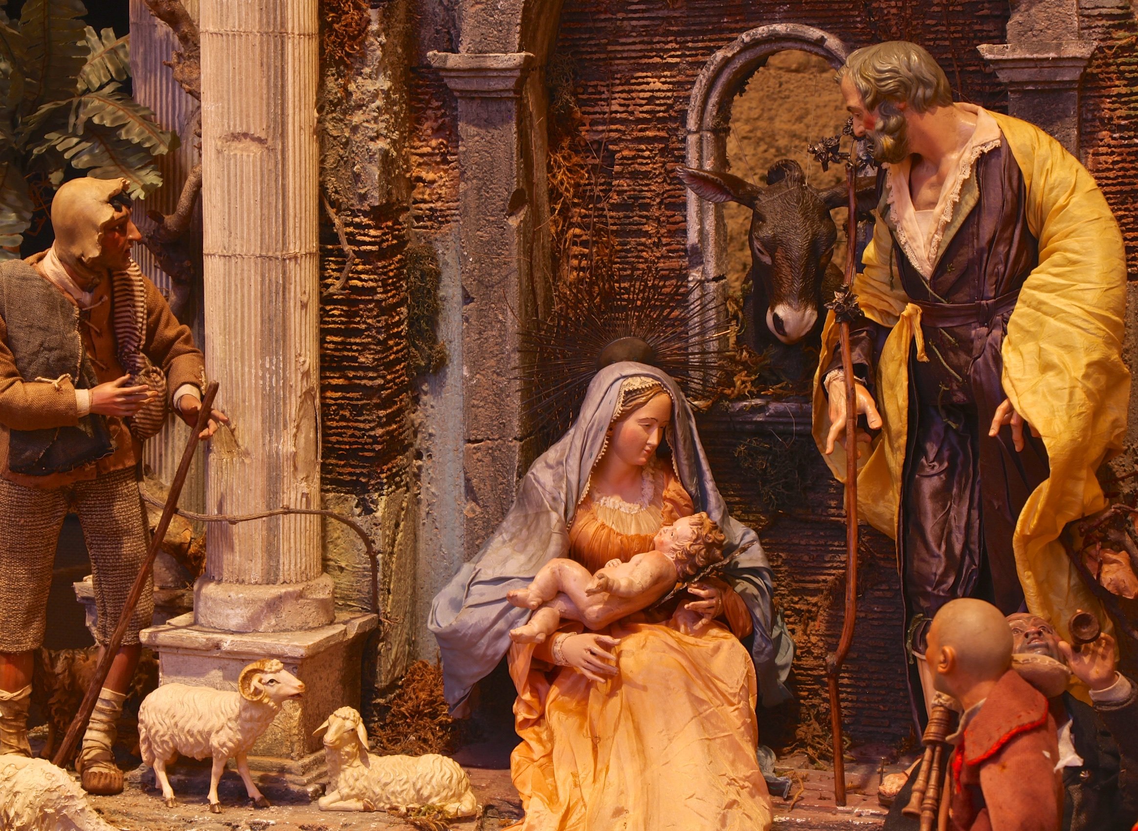  This detail of a Neapolitan Presepio shows the Holy Family amongst stone building ruins. A man can be seen from behind, while in the back a donkey looks on through a window. 