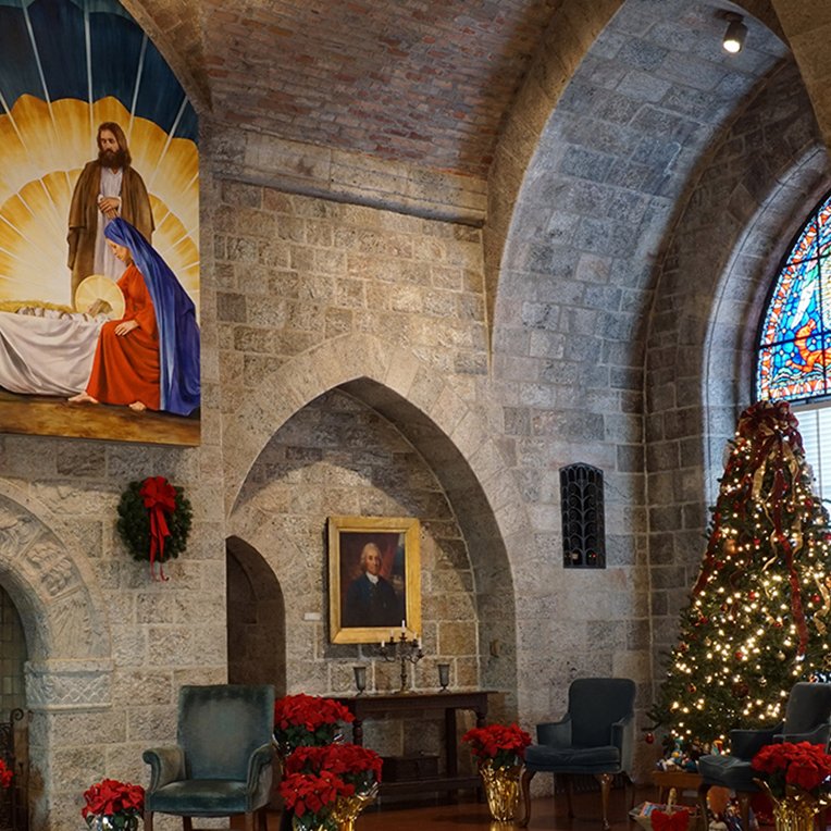  Glencairn Museum’s Upper Hall decorated for Christmas, with a large painting of the Nativity over the fireplace, a decorated Christmas tree, and poinsettias. 