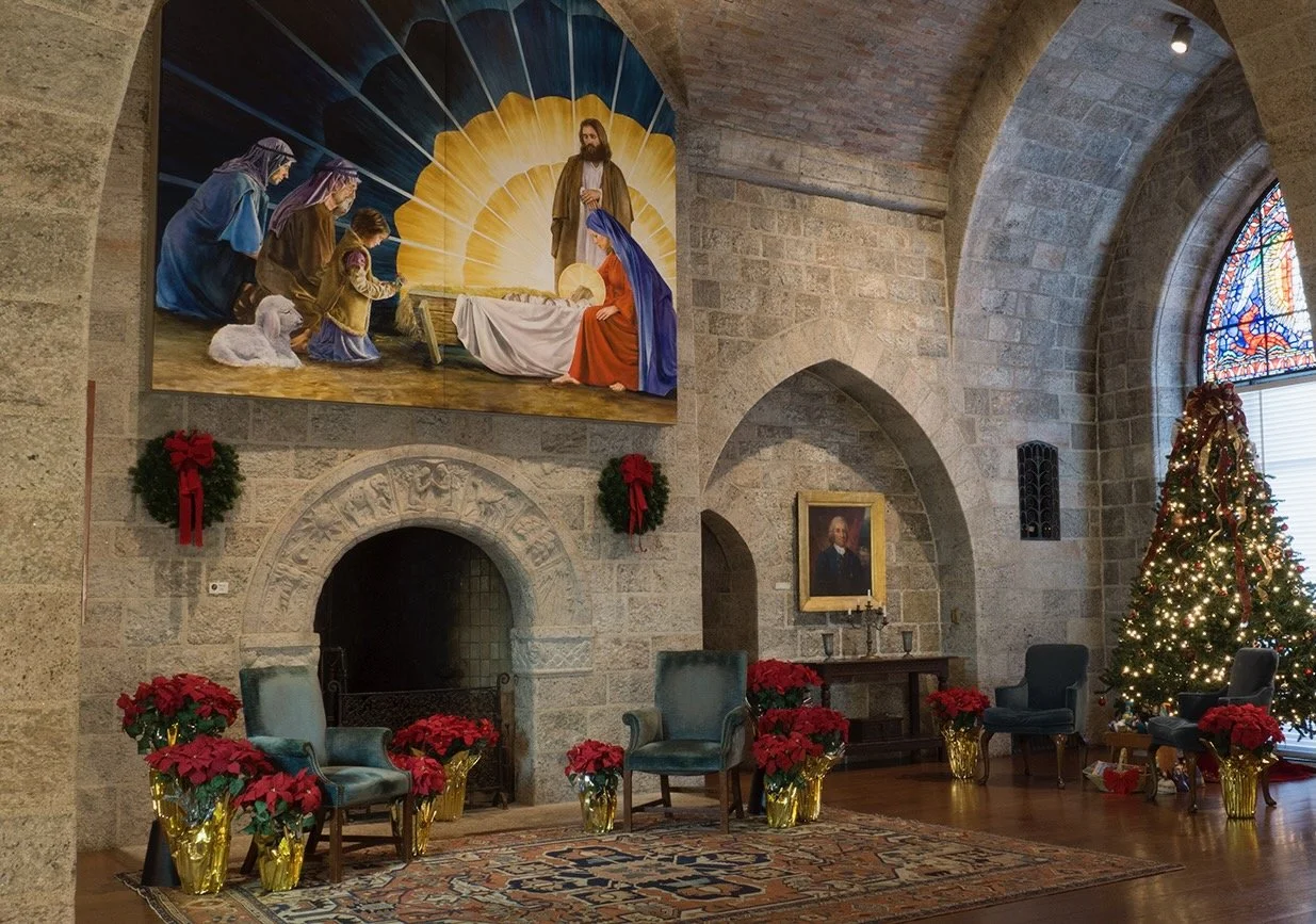 Glencairn Museum’s Upper Hall decorated for Christmas, with a large painting of the Nativity over the fireplace, a decorated Christmas tree, and poinsettias.