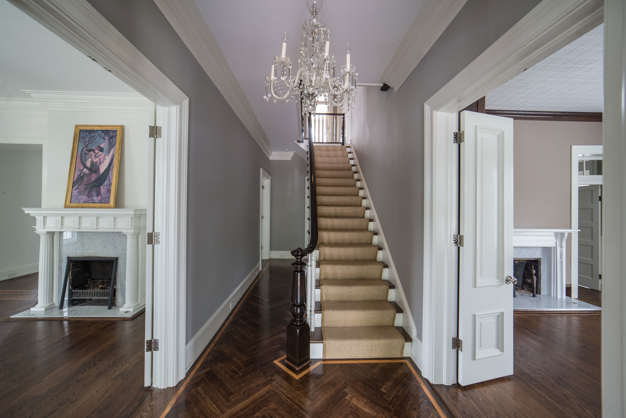 The entry way featuring herringbone hardwood floors flanked on either side by expansive parlors.