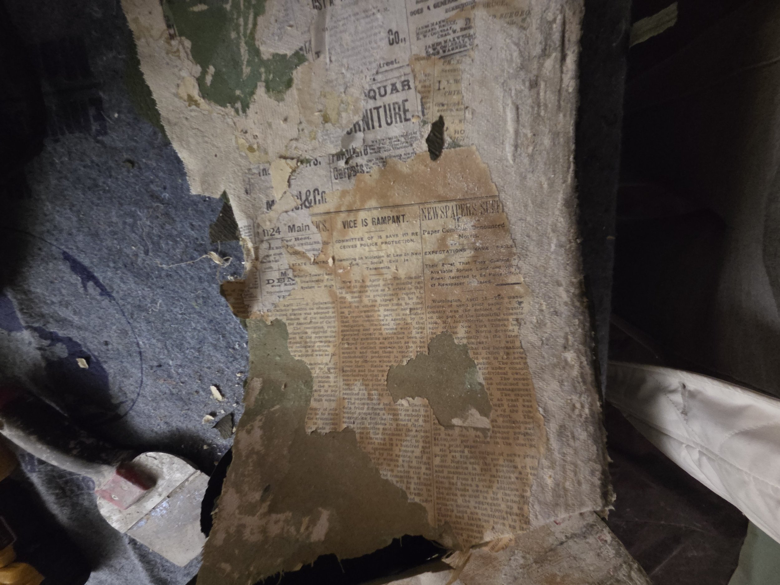 Old, torn newspaper and paper debris layered on a rough wall surface.