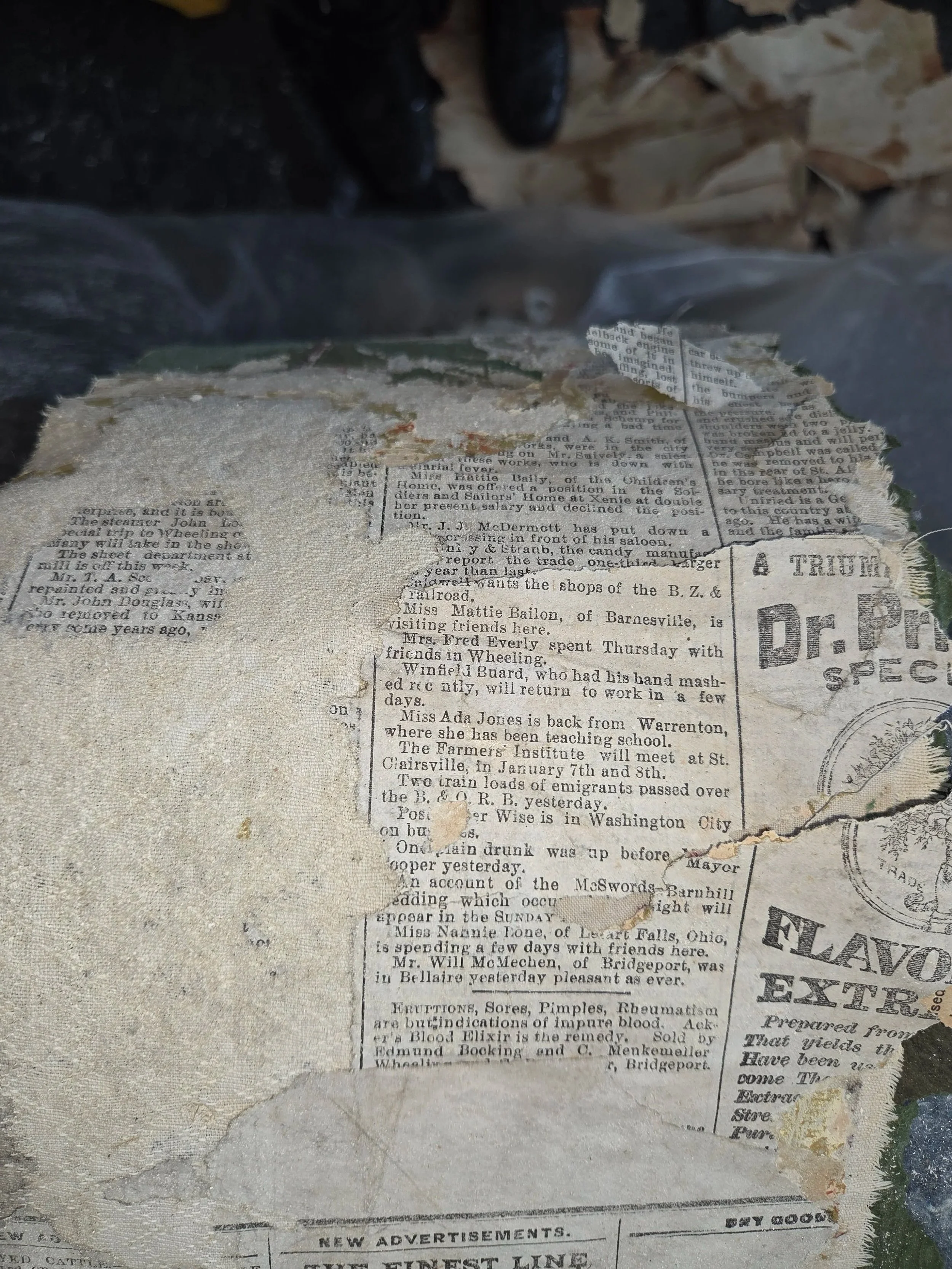 Torn and weathered pieces of old newspaper, with visible text and stamps, some parts torn away or faded.
