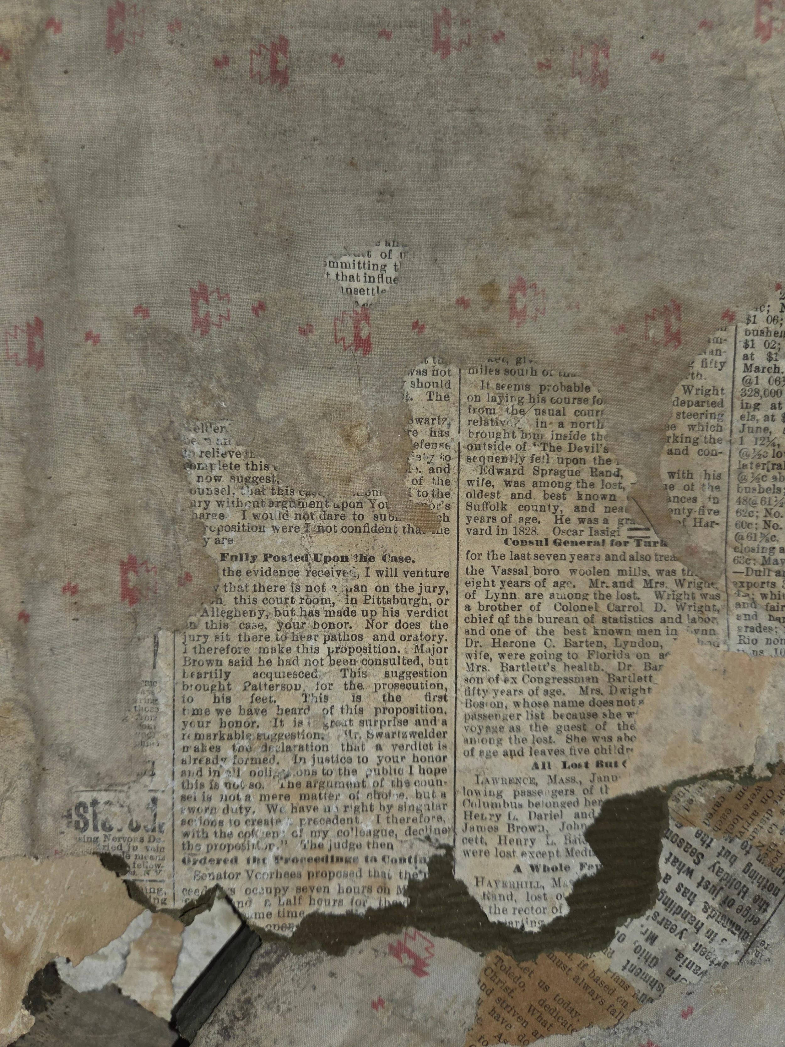 A piece of old, torn newspaper with remnants of text, surrounded by pink patterned designs on a worn, stained fabric surface.