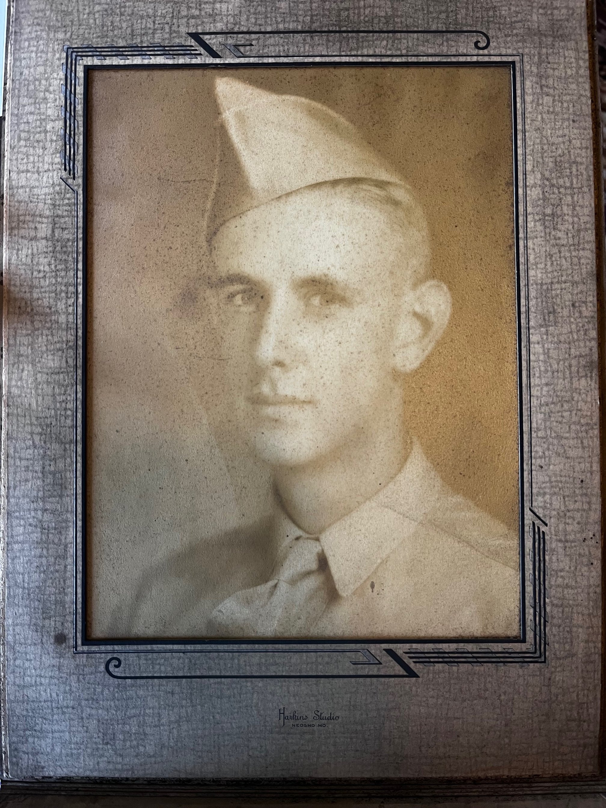 Black and white vintage portrait of a young man in a military uniform and cap, framed in a decorative photo frame.