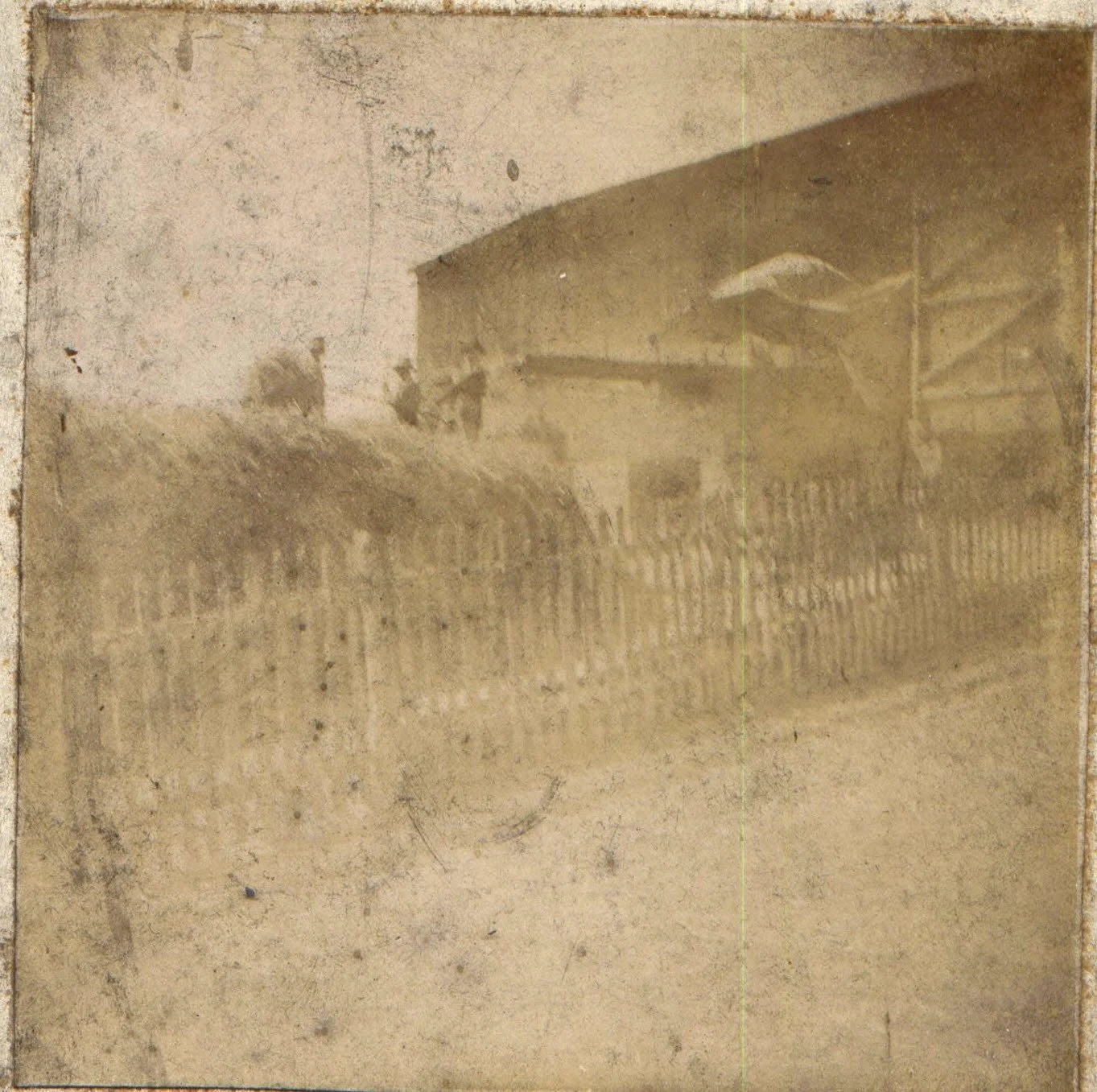An old, sepia-toned photograph showing a traditional rural scene with a horse-drawn cart beside a wooden fence and a barn under a large, arched structure.