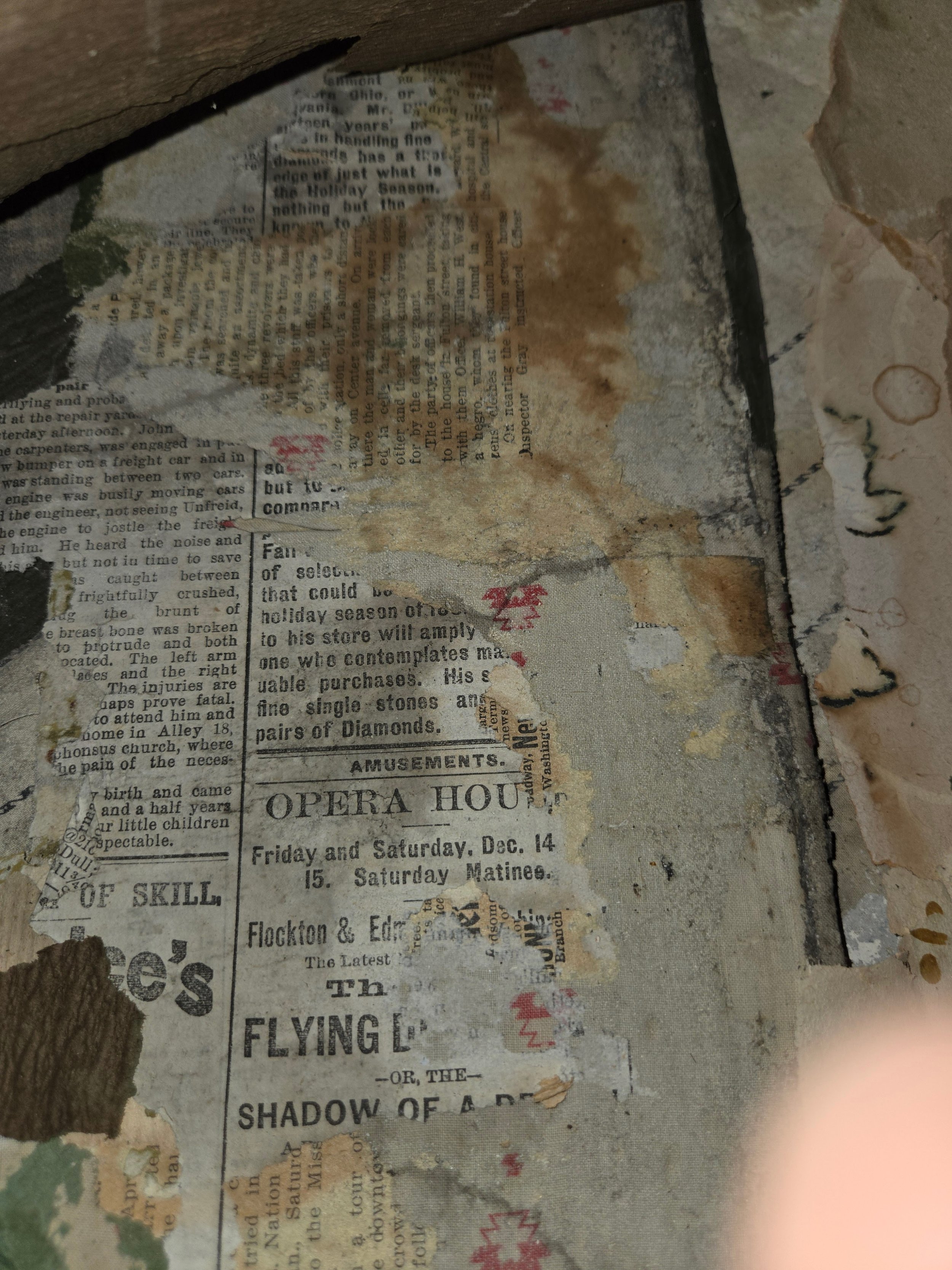 A worn, torn piece of old newspaper with faded and stained text, partially covered by debris and dirt, surrounded by rough, peeling material.