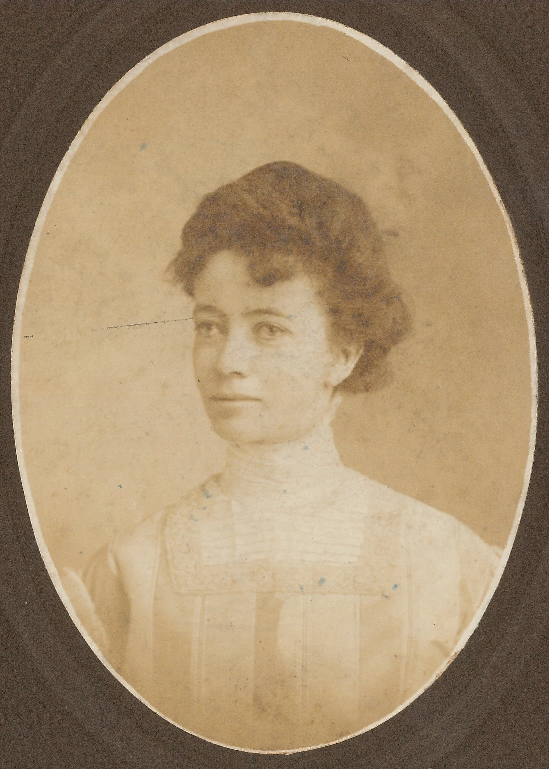 An old sepia-toned portrait photograph of a woman with dark hair styled in an updo, wearing a high-collared blouse or dress with lace detail.
