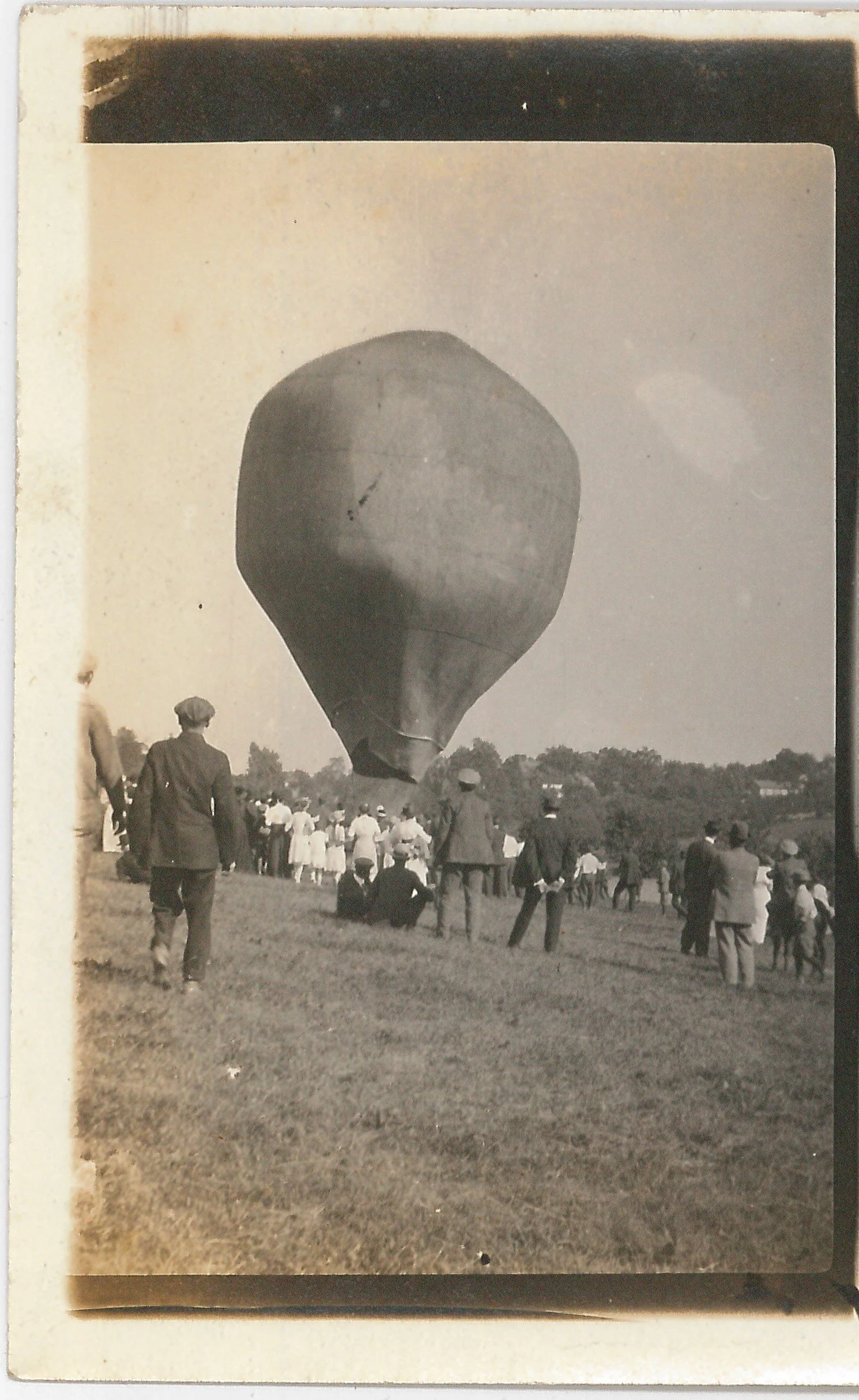 Black and white photo of a hot air balloon about to take flight, with a crowd of people gathered on a grassy field watching.