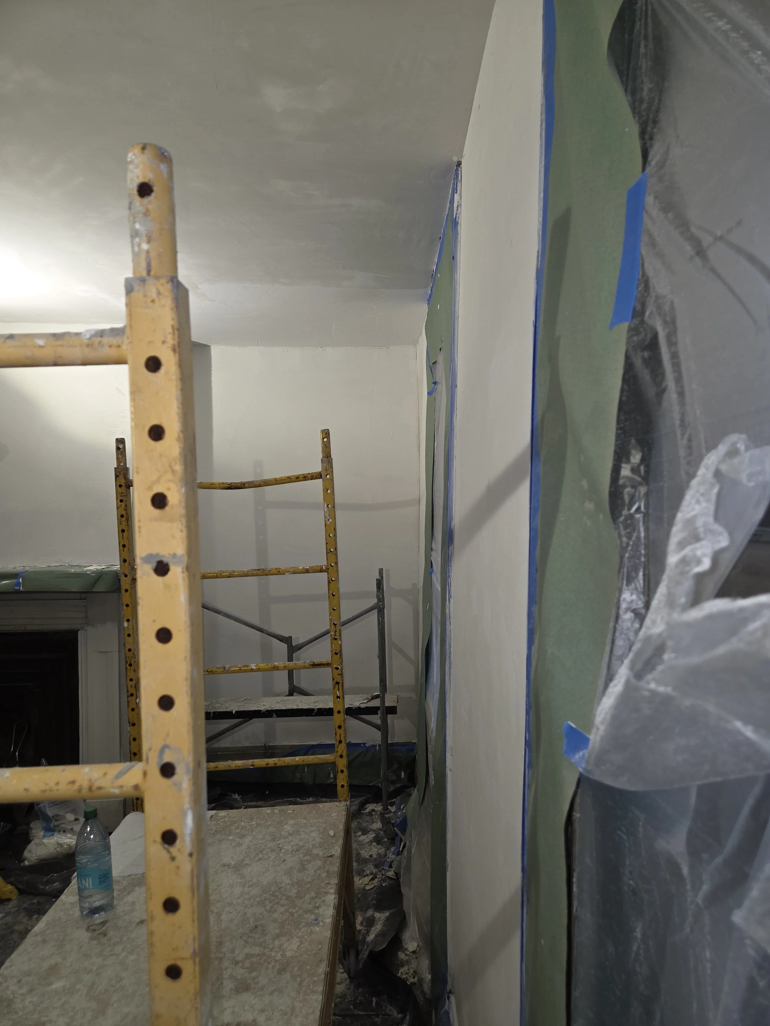 Interior room undergoing renovation, scaffolding and plastic sheeting covering parts of the wall