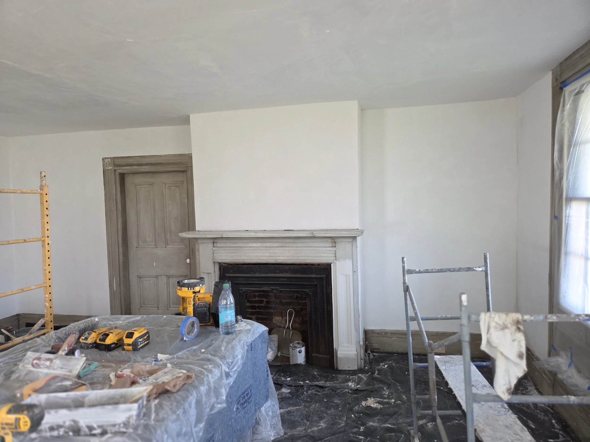 Living room under renovation with tools, scaffolding, and a brick fireplace.