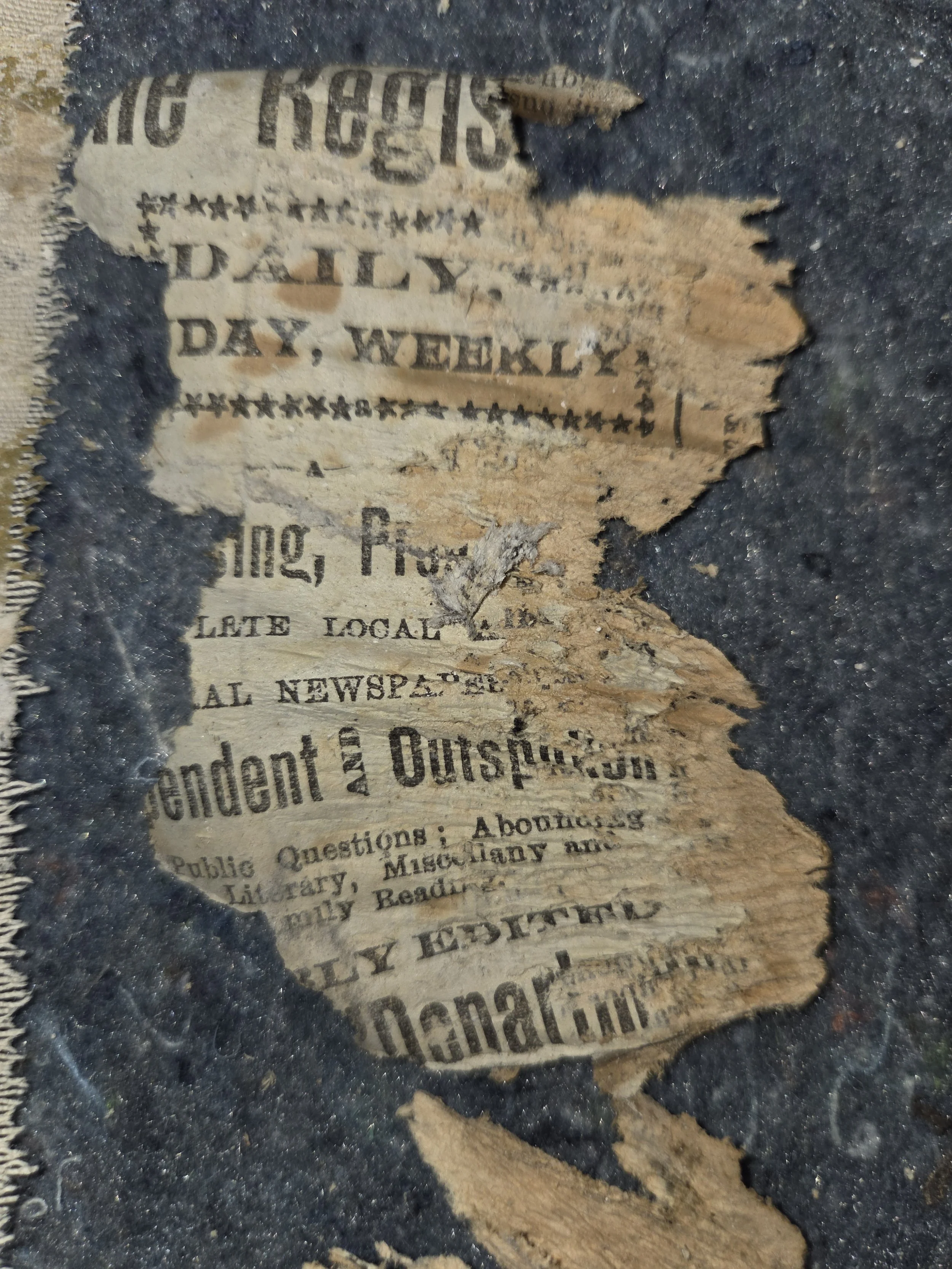A torn and aged newspaper fragment partially embedded in dark soil or debris.