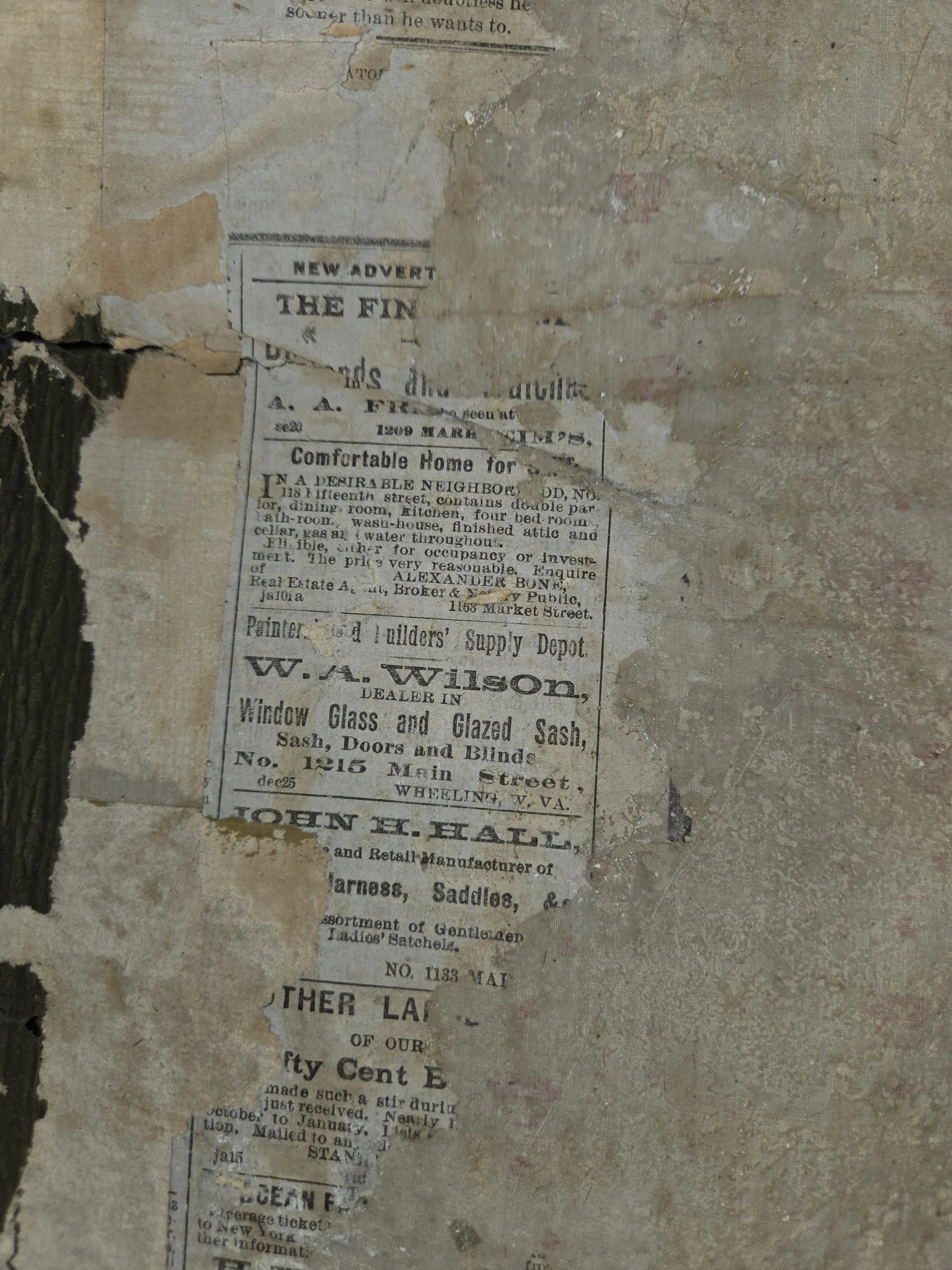 A torn and weathered paper with old newspaper advertisements and articles, partially peeling off a rough, aged wall or surface.