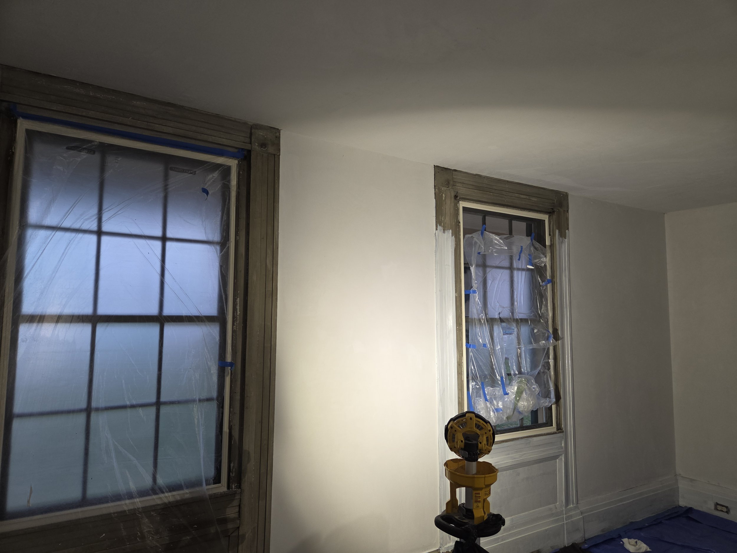 Interior room with two windows covered in plastic, construction tools, and partially painted walls.