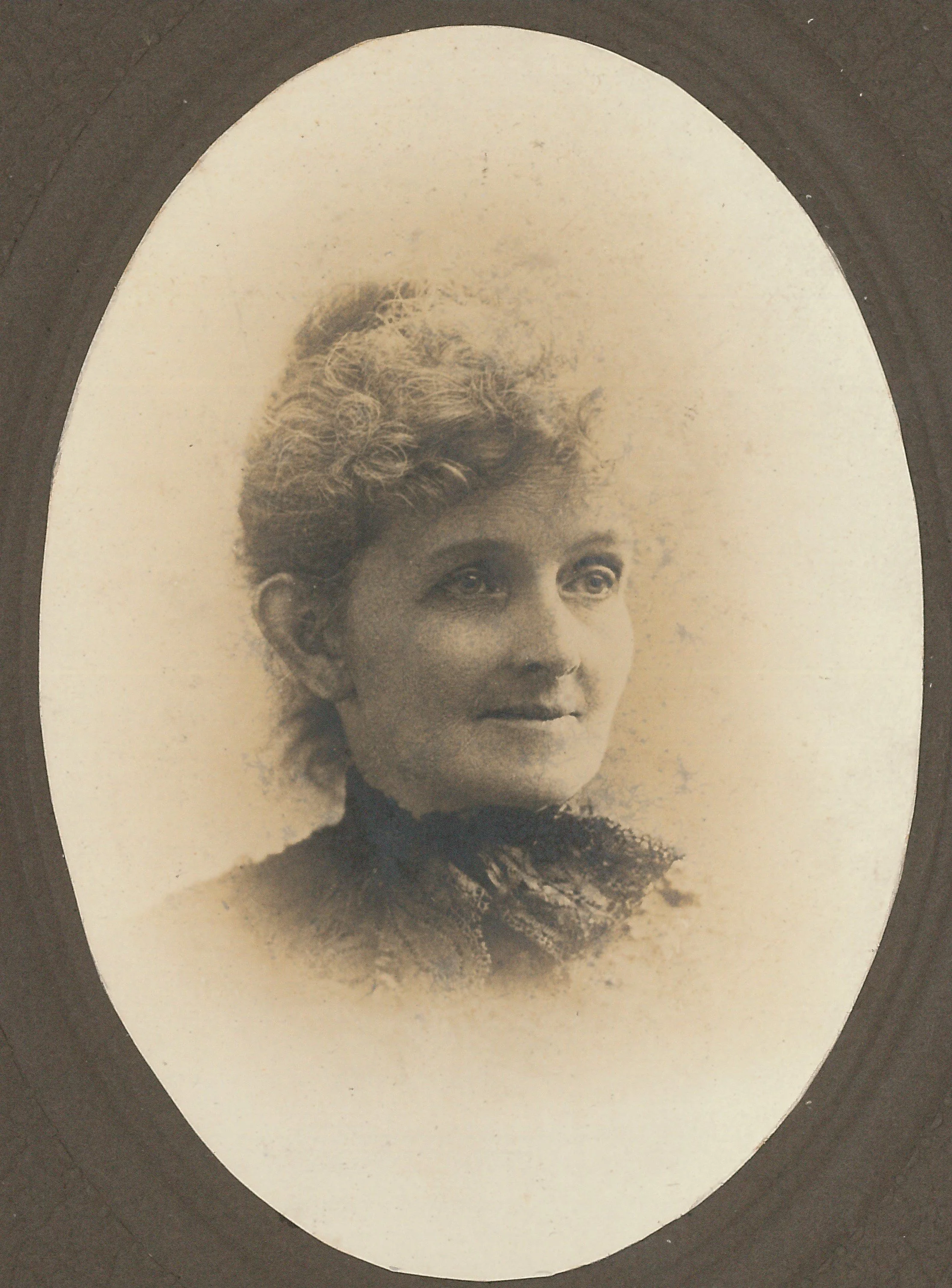 A sepia-toned oval portrait of a woman with curly hair, wearing a dark lace high-collared dress.