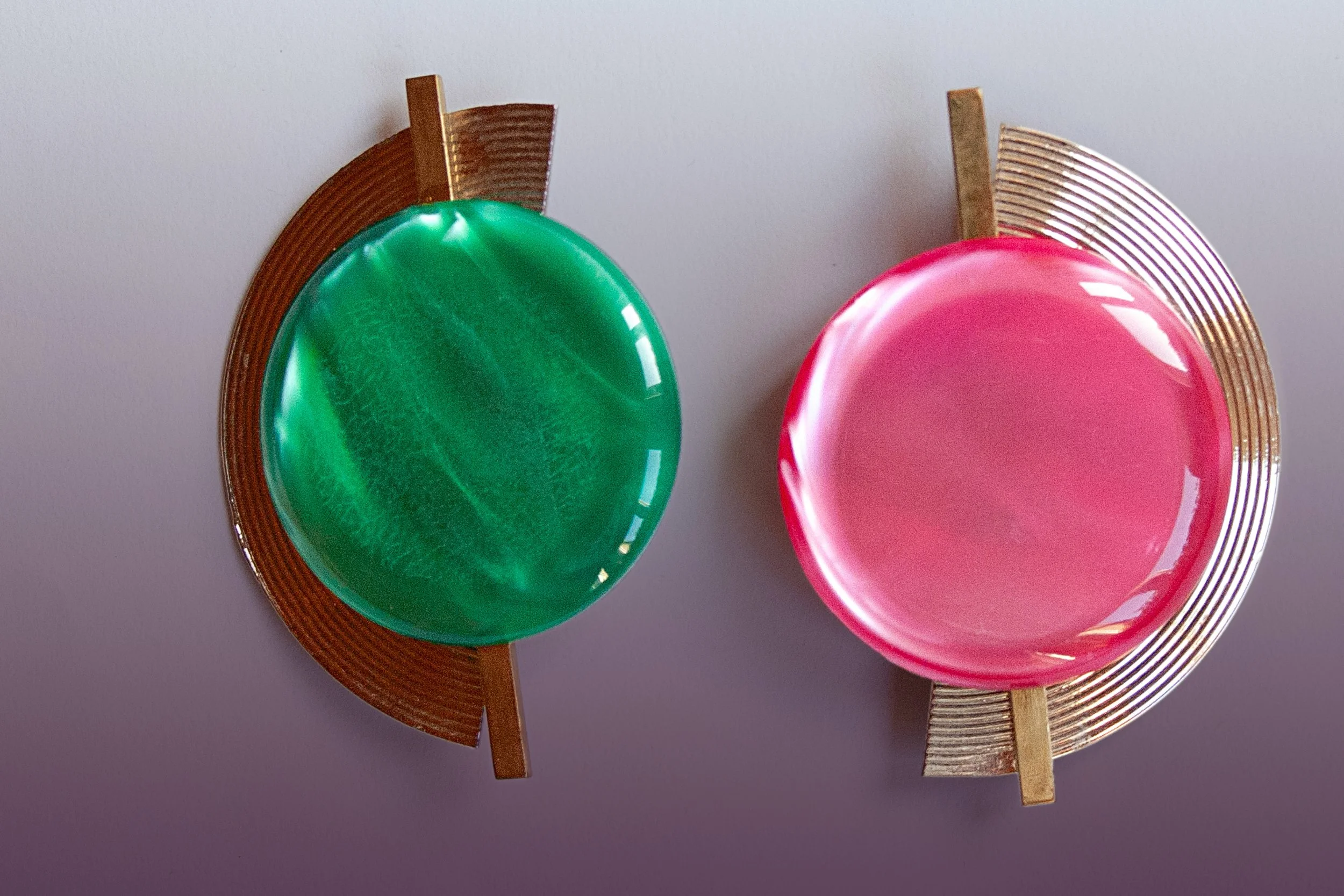 Modeschmuck aus Paris, aus der Mitte des 20.Jahrhundert: zwei Broschen in runder Form in Grün und Pink auf metallener gerippten halbkreisen.