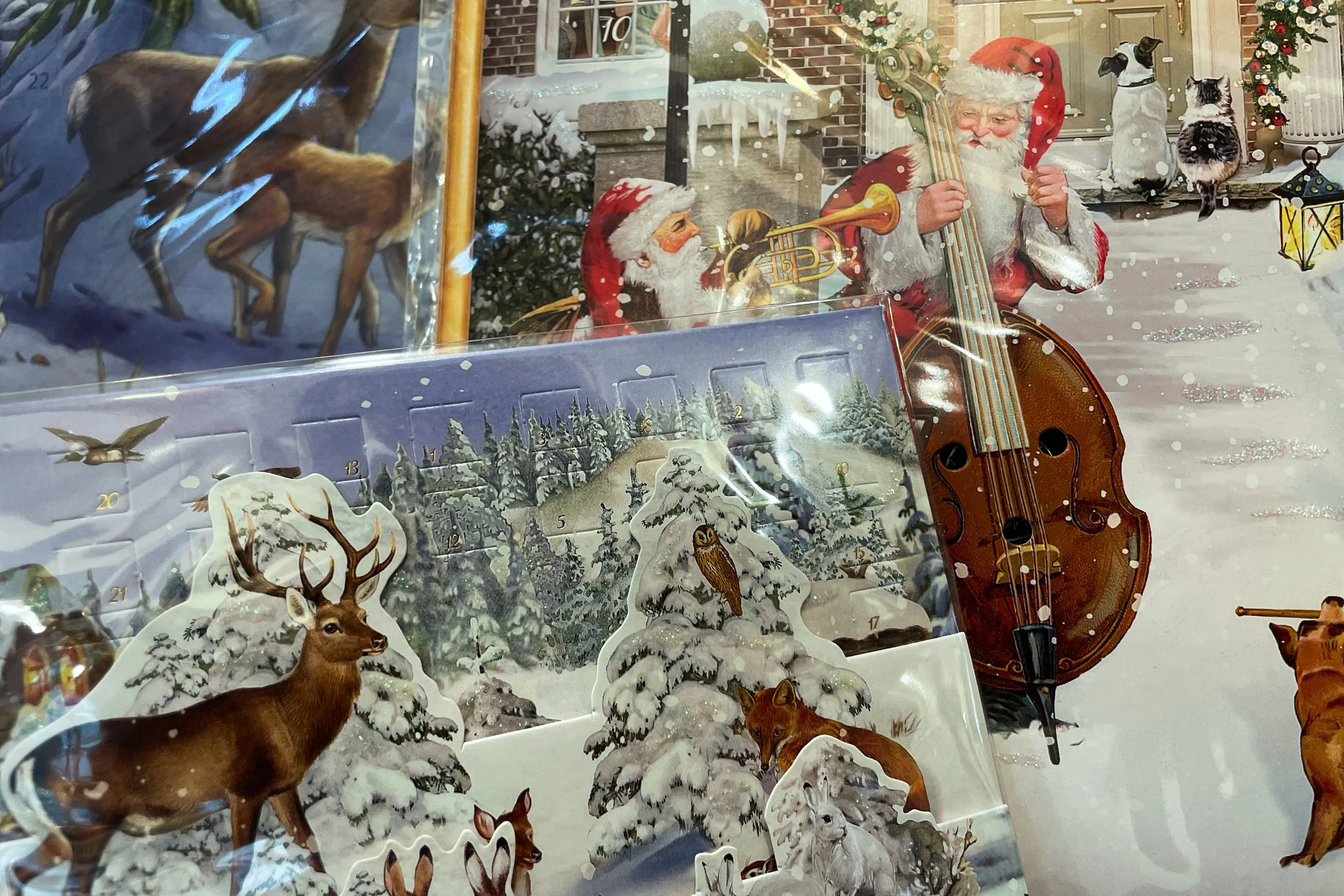 Kalender mit weihnachtlichen und winterlichen Szenen. 24 Türchen und reich mit Glimmer versehen. Einige Kalender sind 3D aufklappbar. Dargestellt sind verschneite Landschaften mit Reh, Hirsch und Waldtieren, sowie ein musizierender Nikolaus in einer 