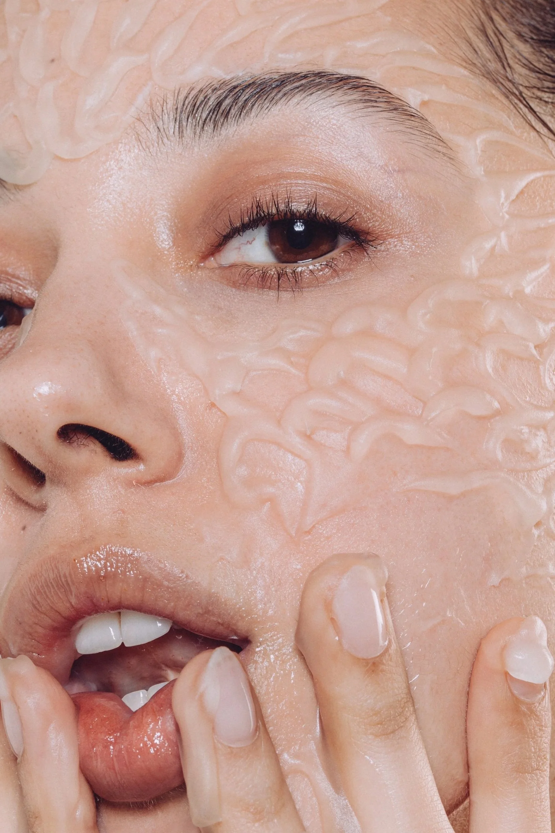 Close-up of a woman with a intricate skincare textures over her face that have been placed to look like feathers, touching her lips and face with her fingers.