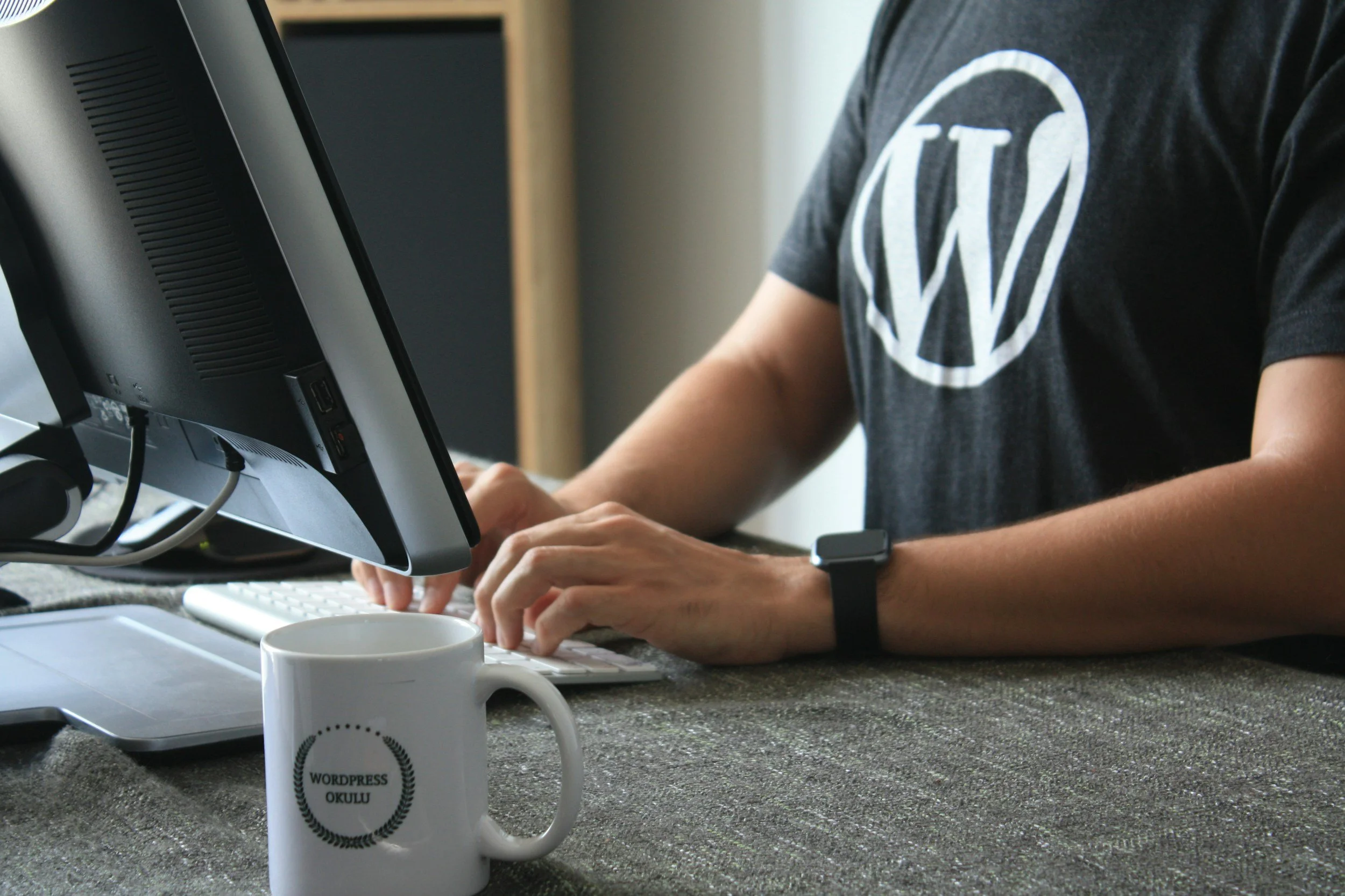T-Shirt mit großem W für WordPress, Mann, zwei Arme an Tastatur