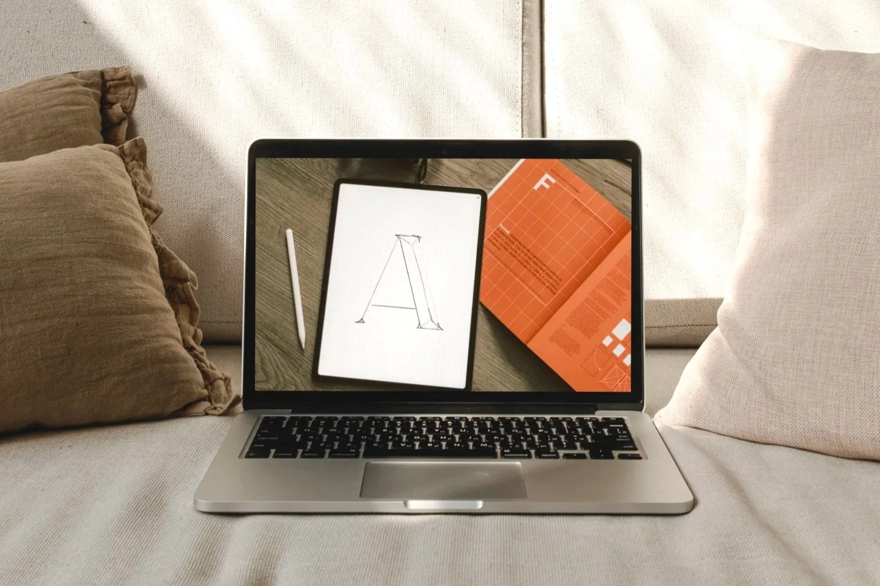 Macbook steht auf Coach, daneben braunes und beiges Kssen