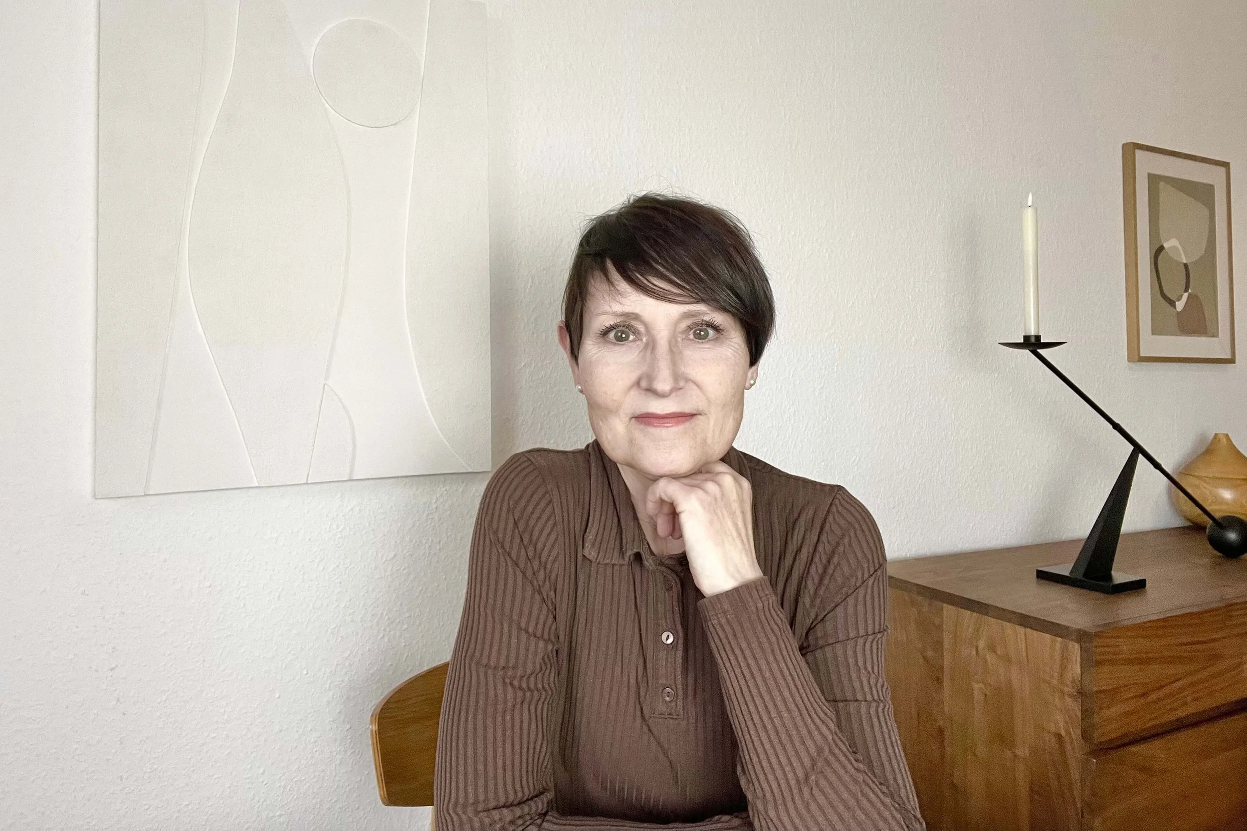 Frau im braunen Poloshirt mit dunklen kurzen Haaren vor Wand mit weißer Leinwand