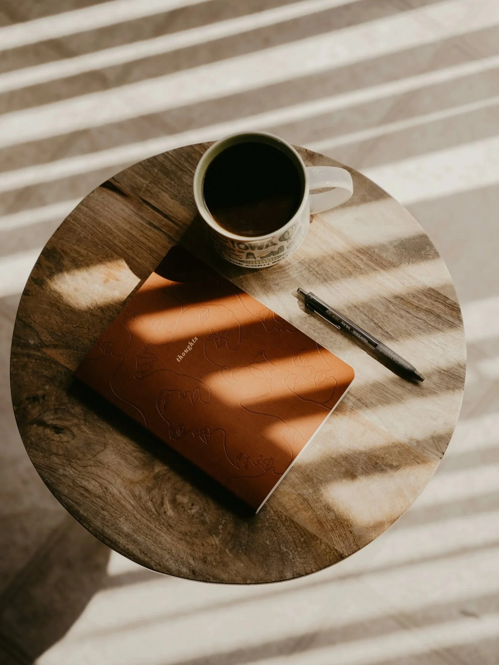 Notizbuch in braun liegt auf rundem Holztisch, daneben eine Kaffeerasse