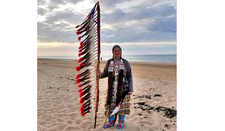 Command Sergeant Major Julia Kelly (U.S. Army retired), one of 80 Native American delegates to the 75th anniversary observance of D-Day, stands on Omaha Beach. Kelly holds an eagle feather staff, an American Indian symbol of respect, honor, and patriotism. (Courtesy of Julia Kelly)