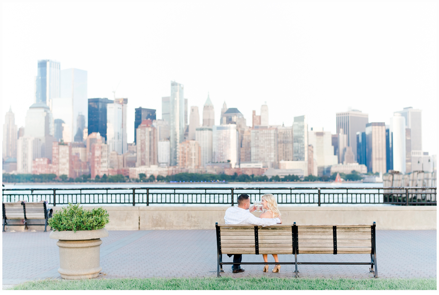 engaged couple sitting on bench at liberty state park