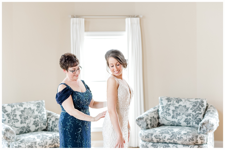 mom helping bride put on wedding dress