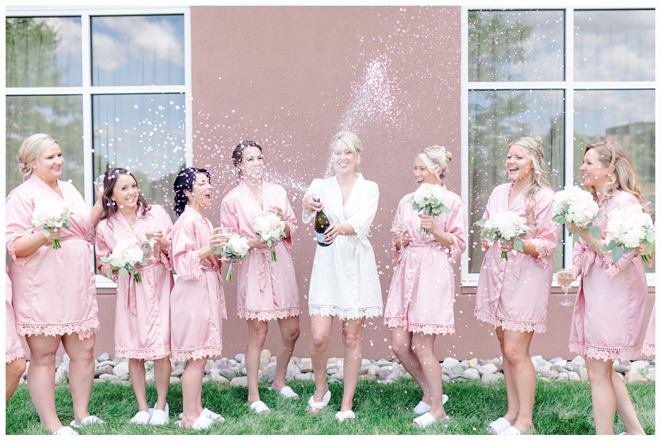 bride and bridemaids in pink silk robes popping champagne