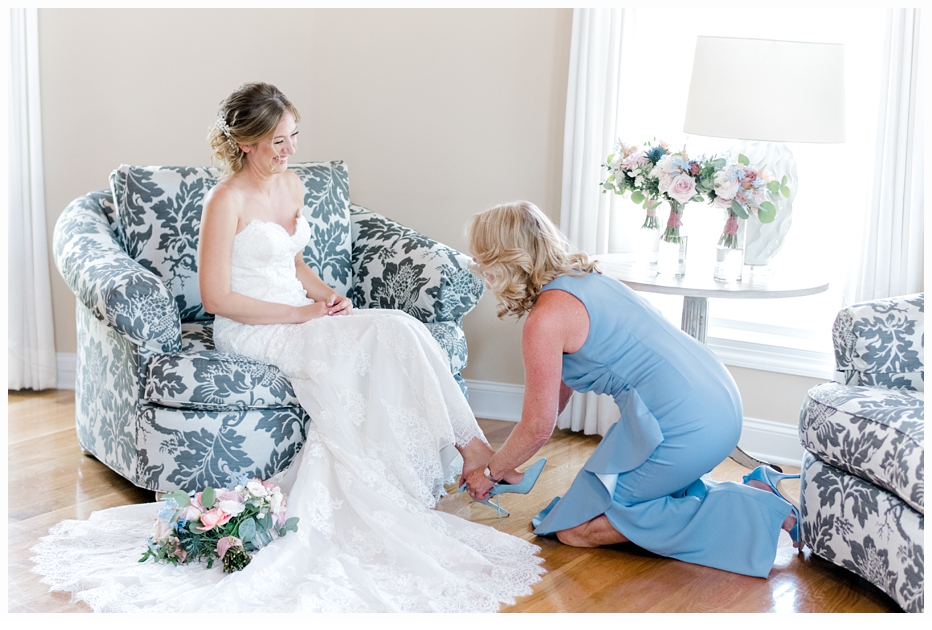 mother helping bride on with her wedding shoes