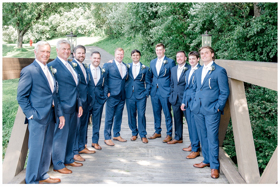 groom and groomsmen standing on bridge on wedding day wearing blue suits