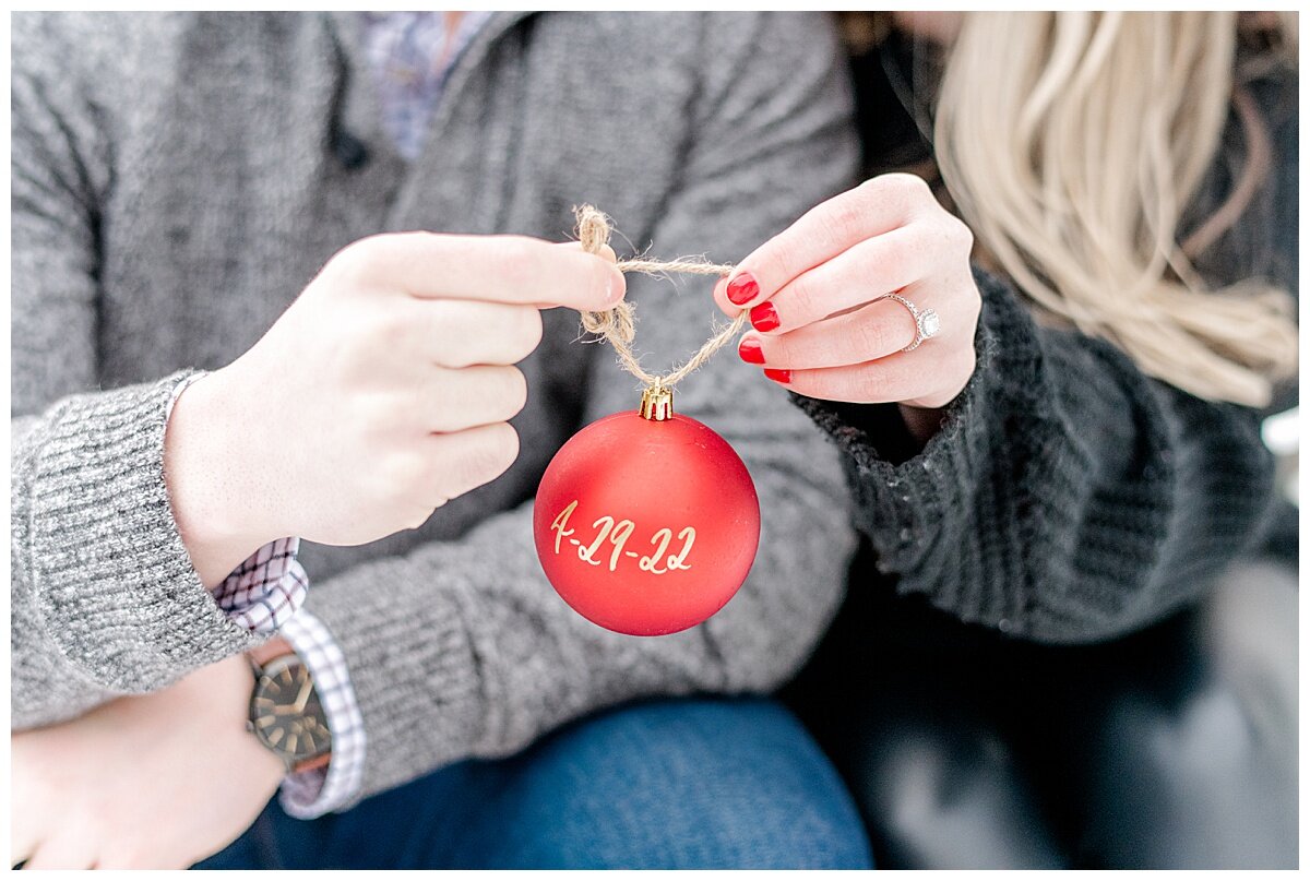 engaged couple holding a red ornament with wedding date written on it