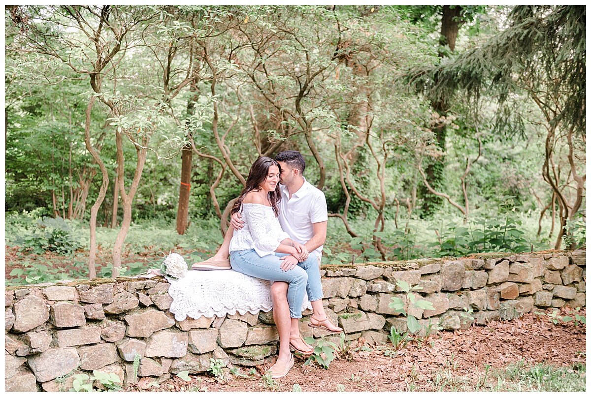 engaged couple sitting on a stone wall