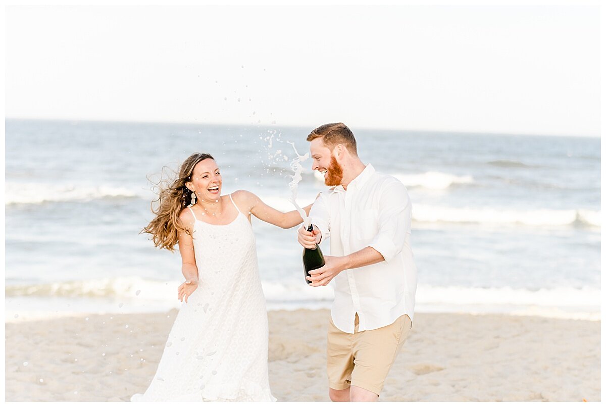 engaged couple popping champagne on the beach