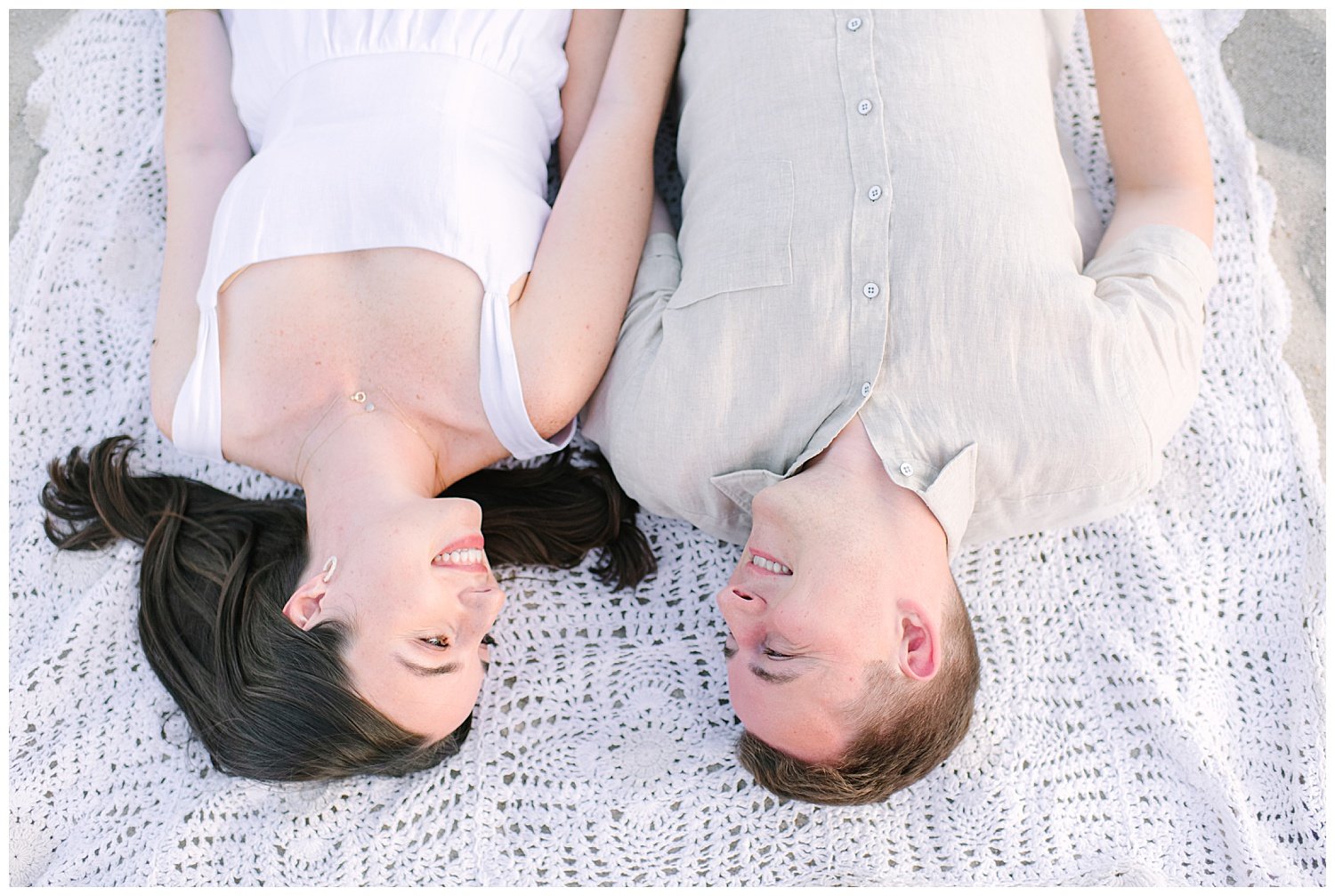 engaged couple laying on a beach blanket smiling