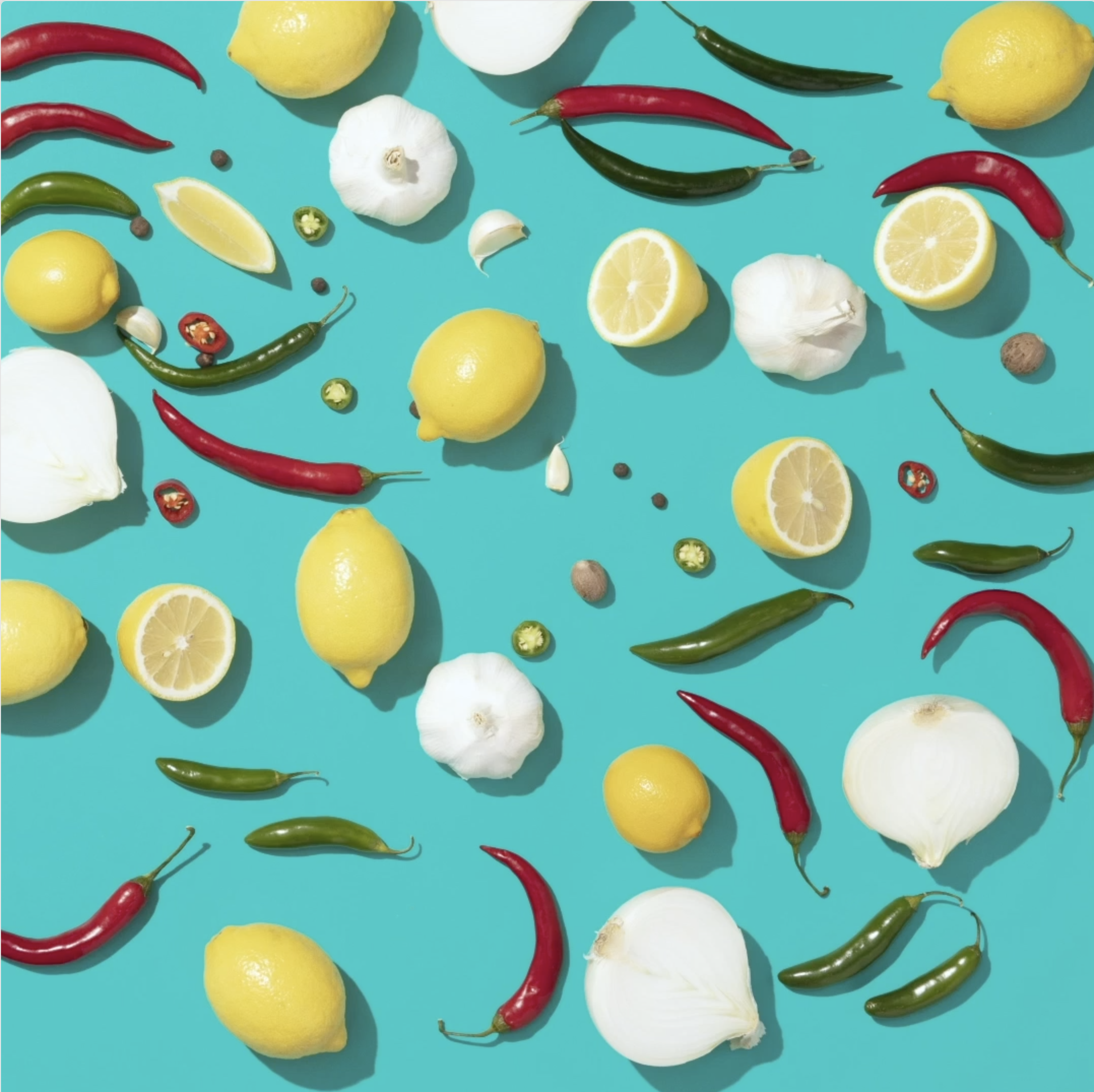 Lemons, red and green chili peppers, garlic, and allspice scattered on a turquoise background.
