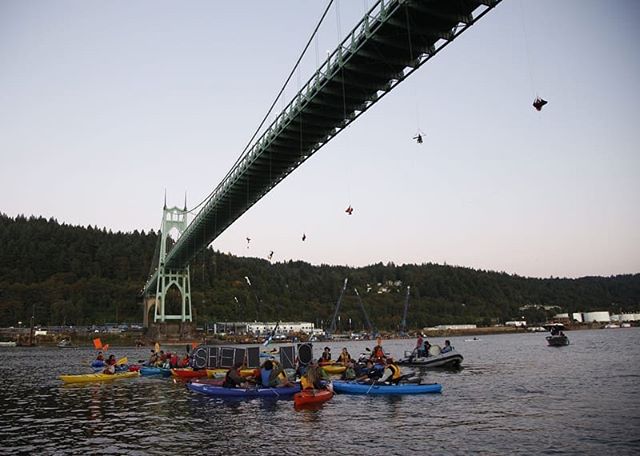 “What’s going on?” I ask.
“They’re deploying,” someone says.
I nod, not knowing what they mean. I’m not sure if anyone at this point realizes exactly what is going on. Eventually it’s clear there’s more than banners in the beams of flashlights in midair beneath the bridge - someone was rappelling down. Over the next few minutes, more headlamps flash in the darkened space above the river. Everyone cheers. The police are already on the bridge. We get the signal and take to the boats.
Chris and I, in an inflatable kayak he purchased specifically for this occasion, are among the first in the water. We paddle out with pride toward the bridge, waiting to see if anyone on the safety team is coming by to give us instructions. The air is charged, electric. Nerves, of course, but they’re overruled by excitement. One of the protectors who had been in Seattle for the blockade of the Polar Pioneer says, “Fuck this doomsday project. In many ways, we’re the last line of defense.”
As we drift upriver toward the bridge, ready to act as the front line of the flotilla, I look up at the lights dangling from the bridge: 14 brave souls from Greenpeace. Not even our organizers knew they were coming. We cheer for them, to them. They cheer in response. I look around at this manifestation of Blockadia; I see people of all backgrounds coming together in solidarity for the latest chapter of this Davids vs Goliath Inc. struggle for our future. I see college students and grandparents; hardened activists and 1st-time demonstrators; "environmentalists" and those who simply want to protect what they love. I see members of my community willingly risking arrest, some of whom have never been in a boat before. I see a movement. I’ve never felt more empowered. I feel tears well in my eyes as I join the chants:
“Portland says:”
“sHell No!”
"Seattle said:”
“sHell No!”
“Alaska said:”
“sHell No!”
“The Duwamish said:”
“sHell No!”
The Reds were going to raft up in the shipping channel, arrange our bows in a star formation, chain our boats together, and drop anchor. In this moment, there was no need. The Fennica wouldn’t be going anywhere with the climbers in place. *tbc*