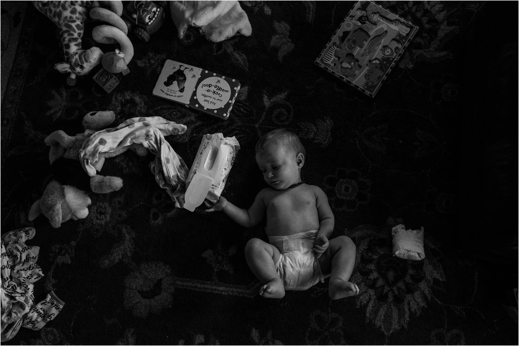 baby laying on the ground surrounded by stuff