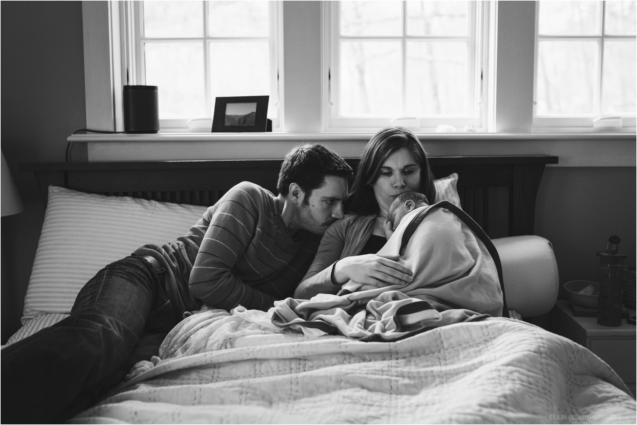 Mom and dad laying in bed holding baby