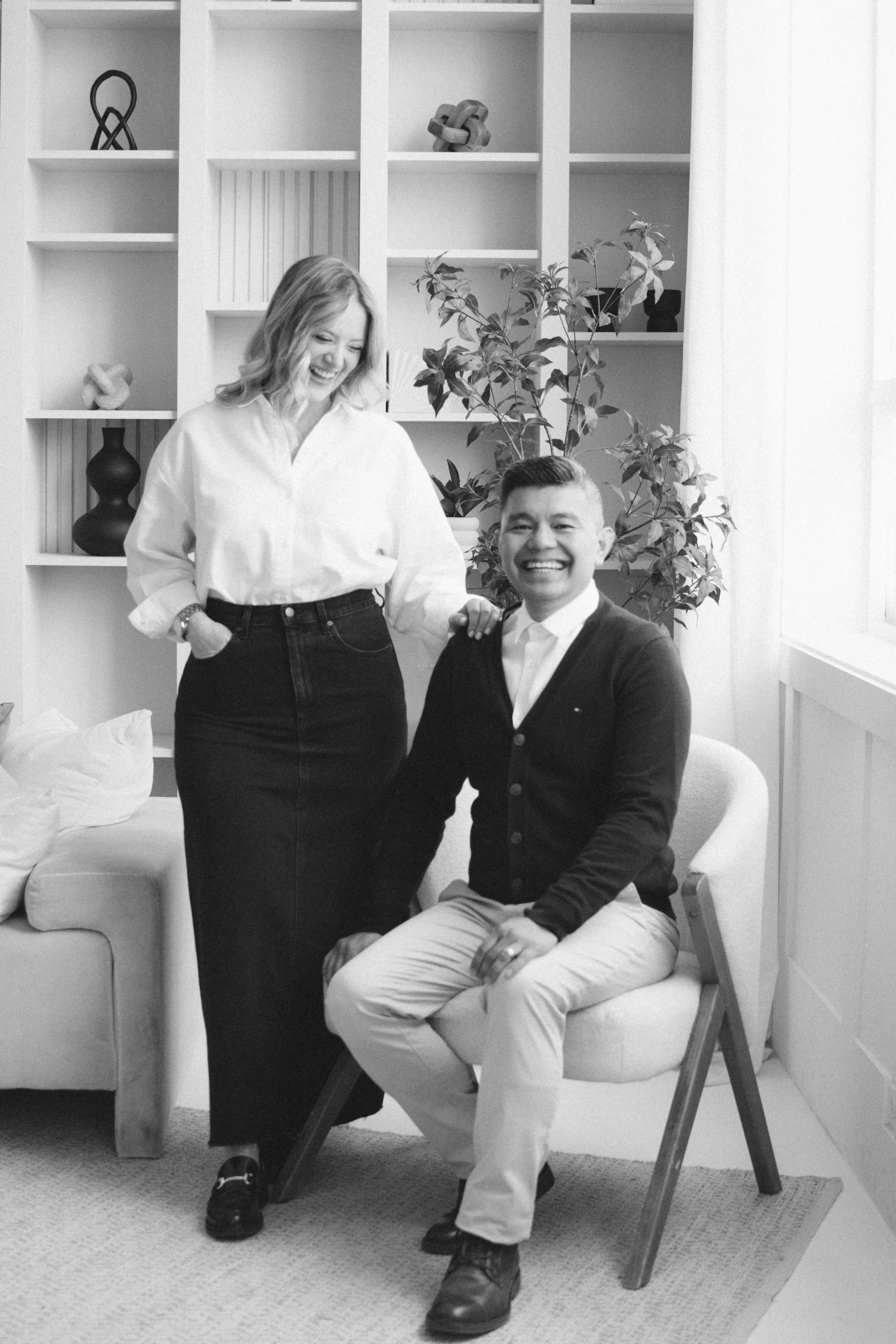 Black and white portrait of husband and wife wedding photographers posing together in a studio