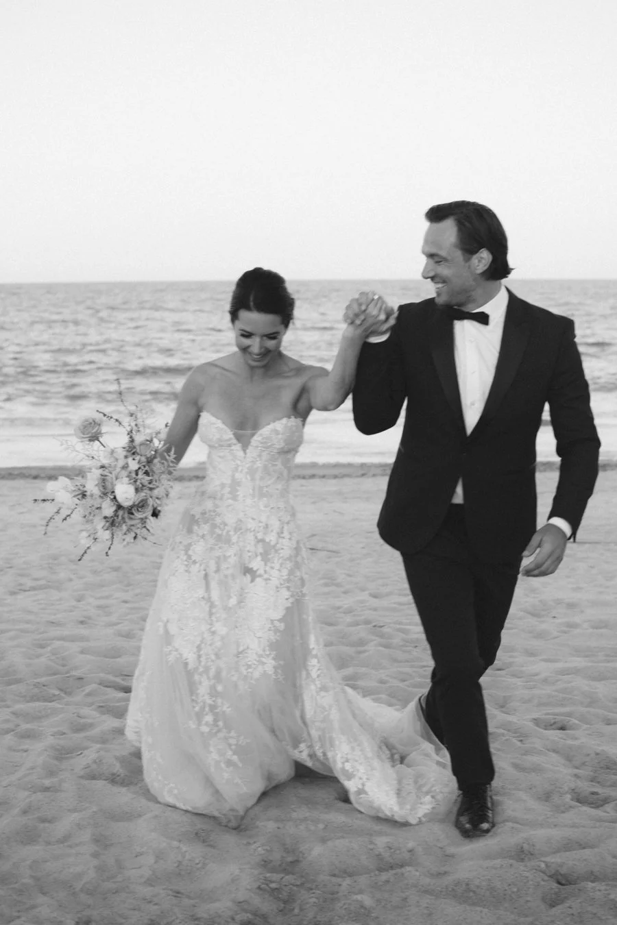 Bride and groom sharing a joyful moment on the beach at their luxury destination wedding.