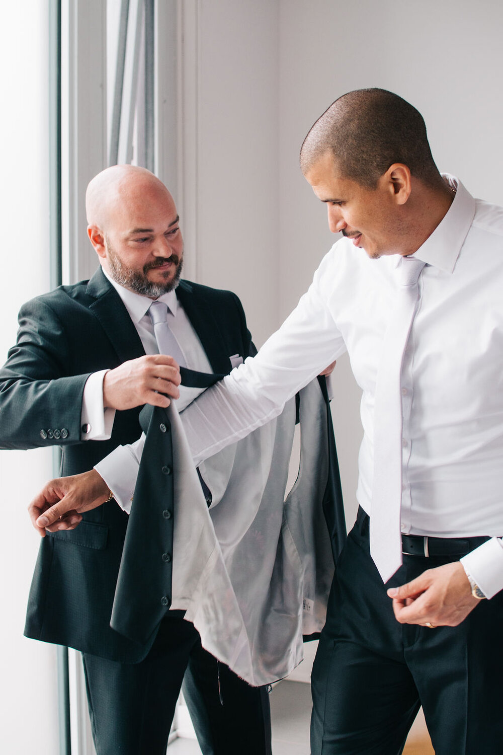 Photograph of best man helping groom get ready on his wedding day