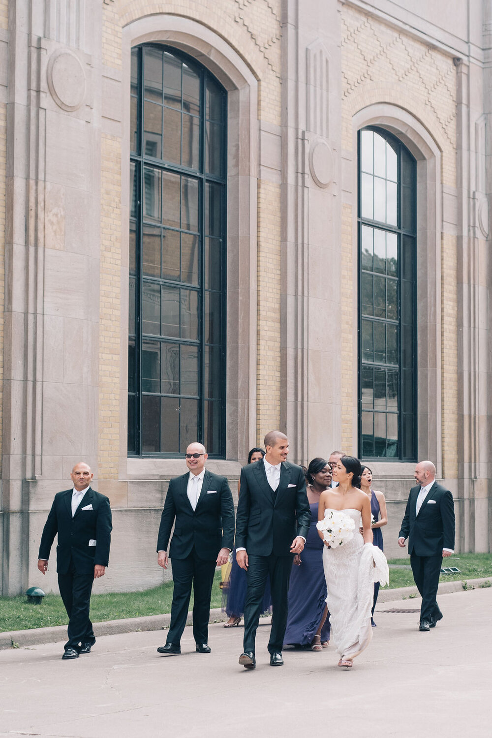 Candid wedding day photograph as Toronto bridal party walk to have their photographs taken at the R.C. Harris Water Treatment Plant 