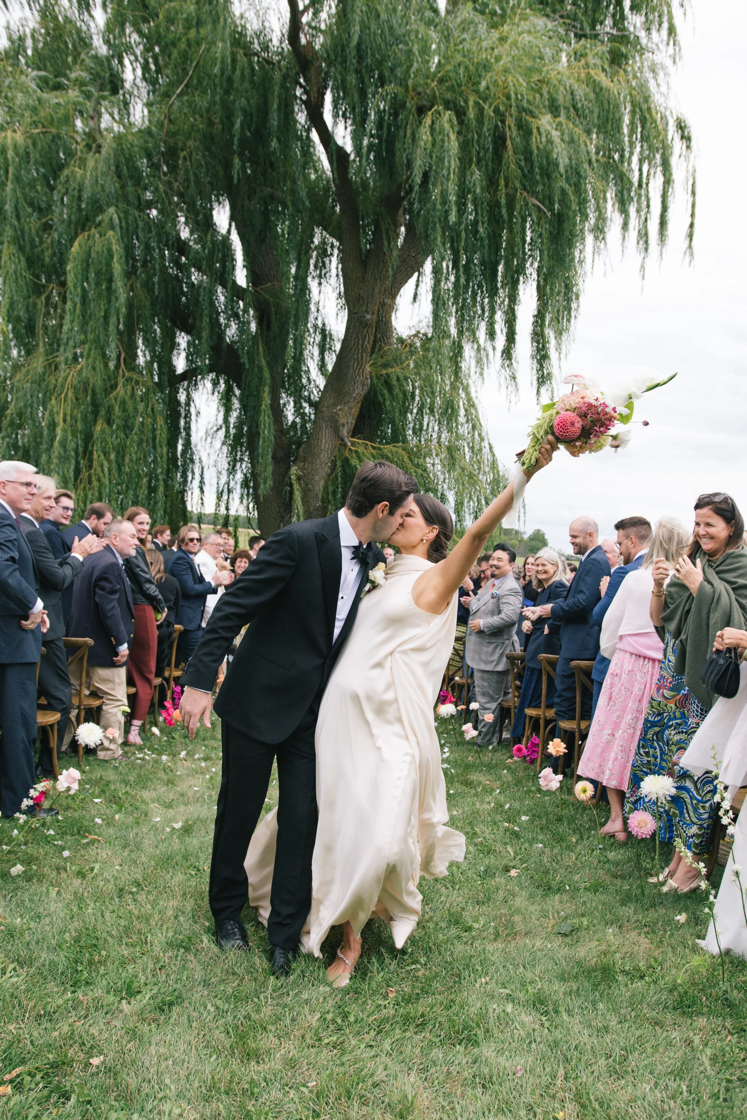 Candid wedding photography of a couple's recessional at a private estate wedding, featuring garden-style floral accents and a scenic countryside backdrop.