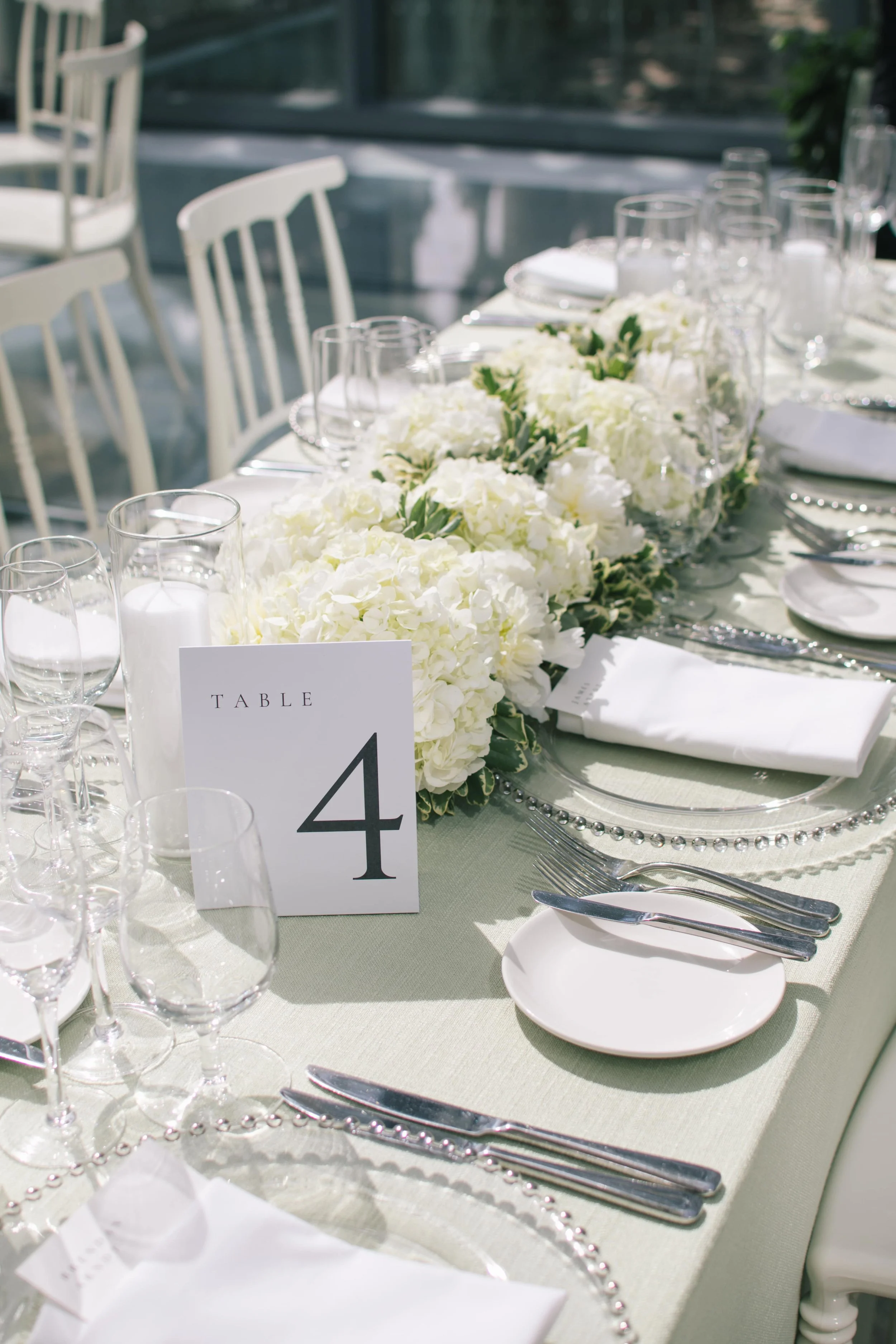 Elegant wedding table setting with white floral centerpiece, glassware, and soft green linens