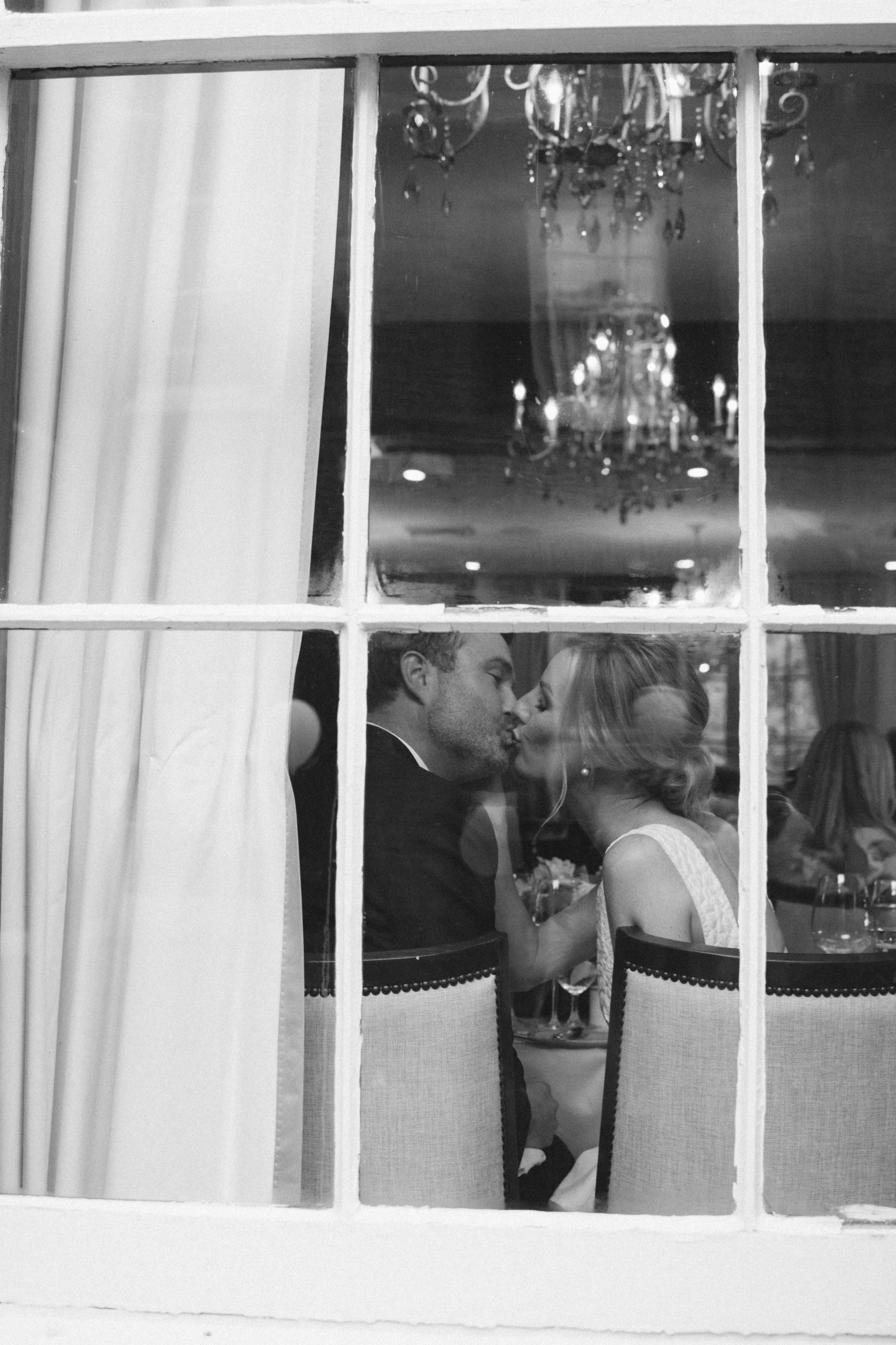 Bride and groom sharing a kiss through a window during their wedding reception