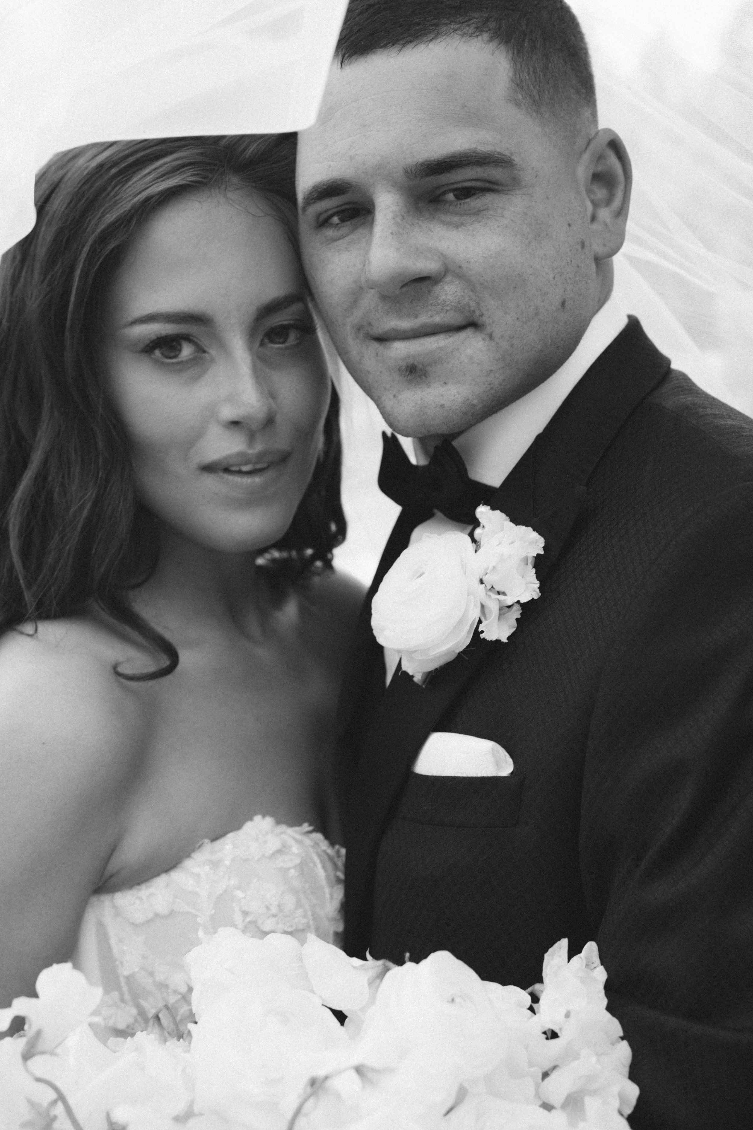 Black and white portrait of a bride and groom under a wedding veil on their wedding day